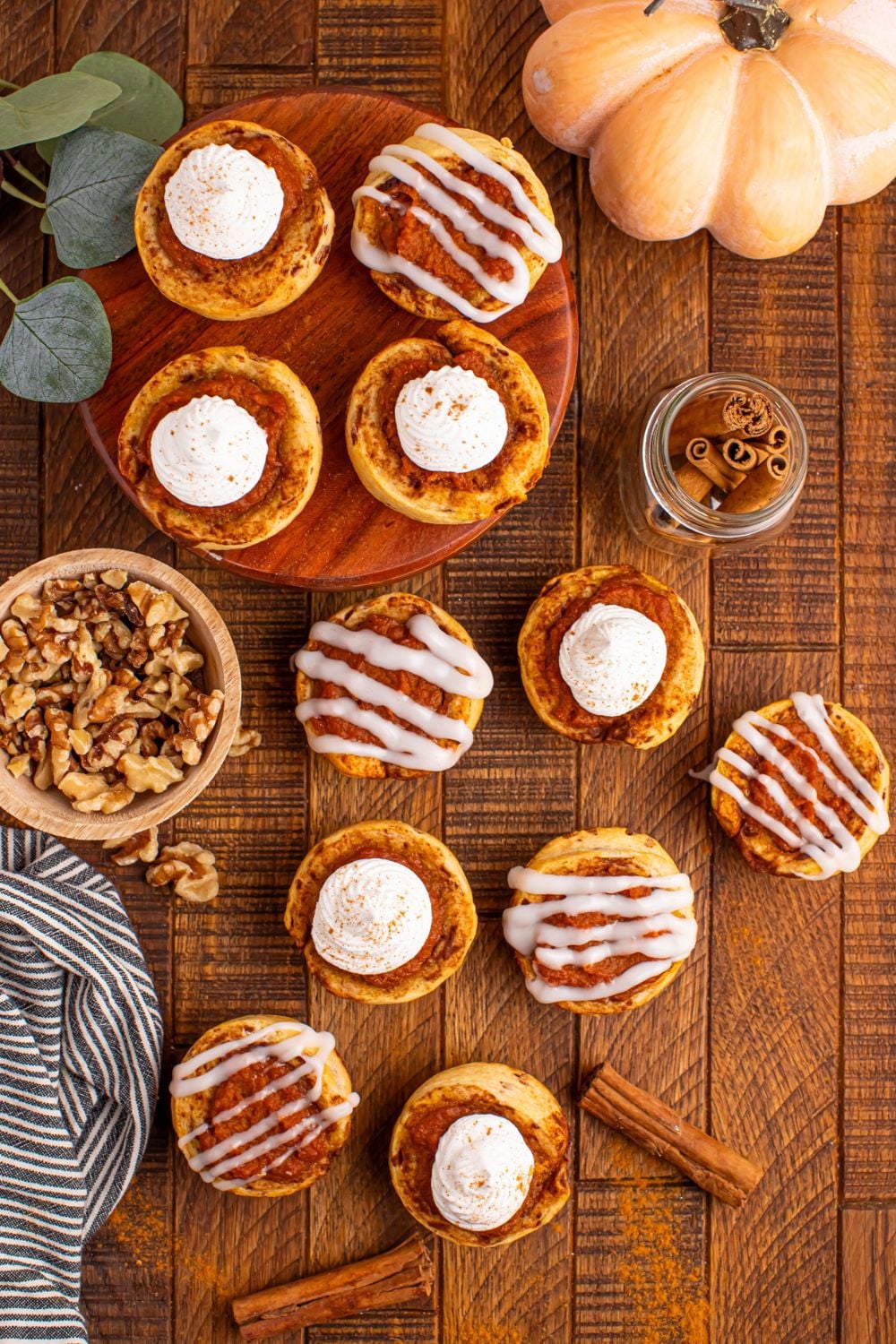 overhead look of table full of Pumpkin Pie Cinnamon Roll Cups spread all over and a pumpkin to side and ingredients in small bowls
