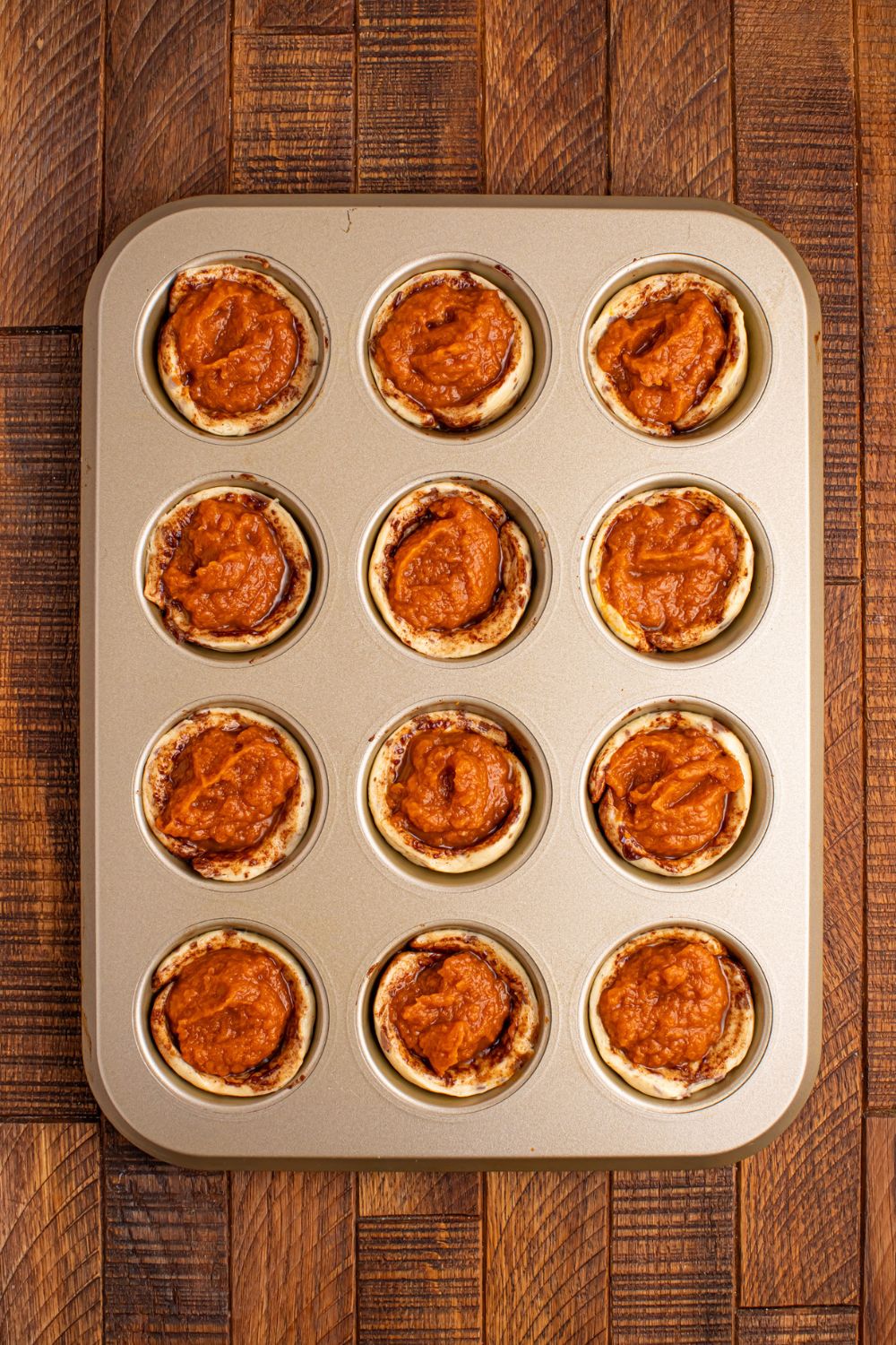 raw Pumpkin Pie Cinnamon Roll Cups sitting in muffin tin on table