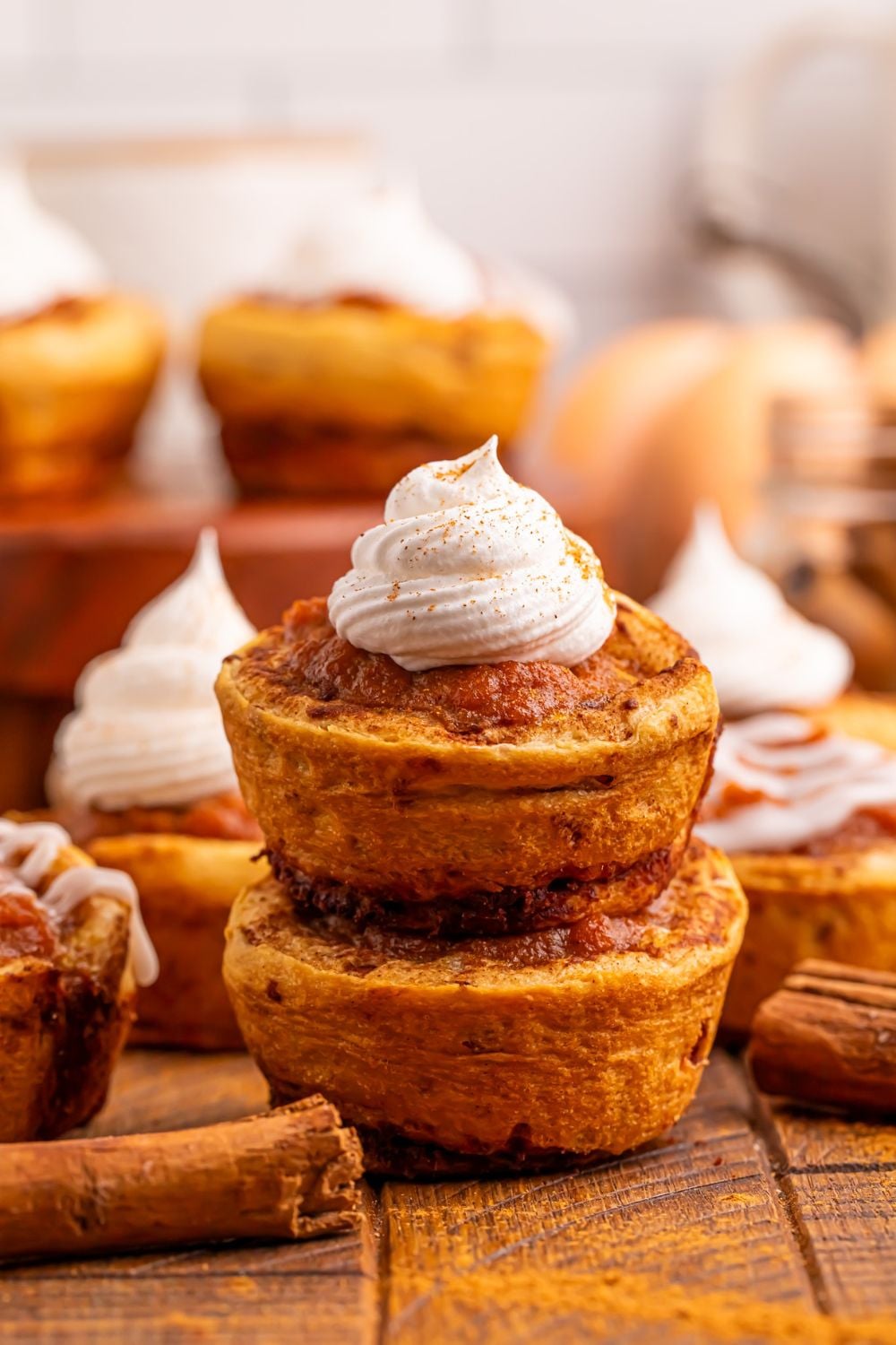 Pumpkin Pie Cinnamon Roll Cups stacked on table with a bunch of cups spread over table