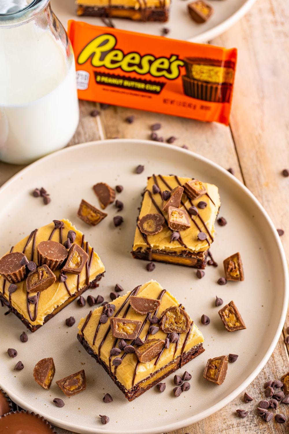 Reeses Stuffed Brownies on a plate with a container of Reese's in the background and a glass of milk