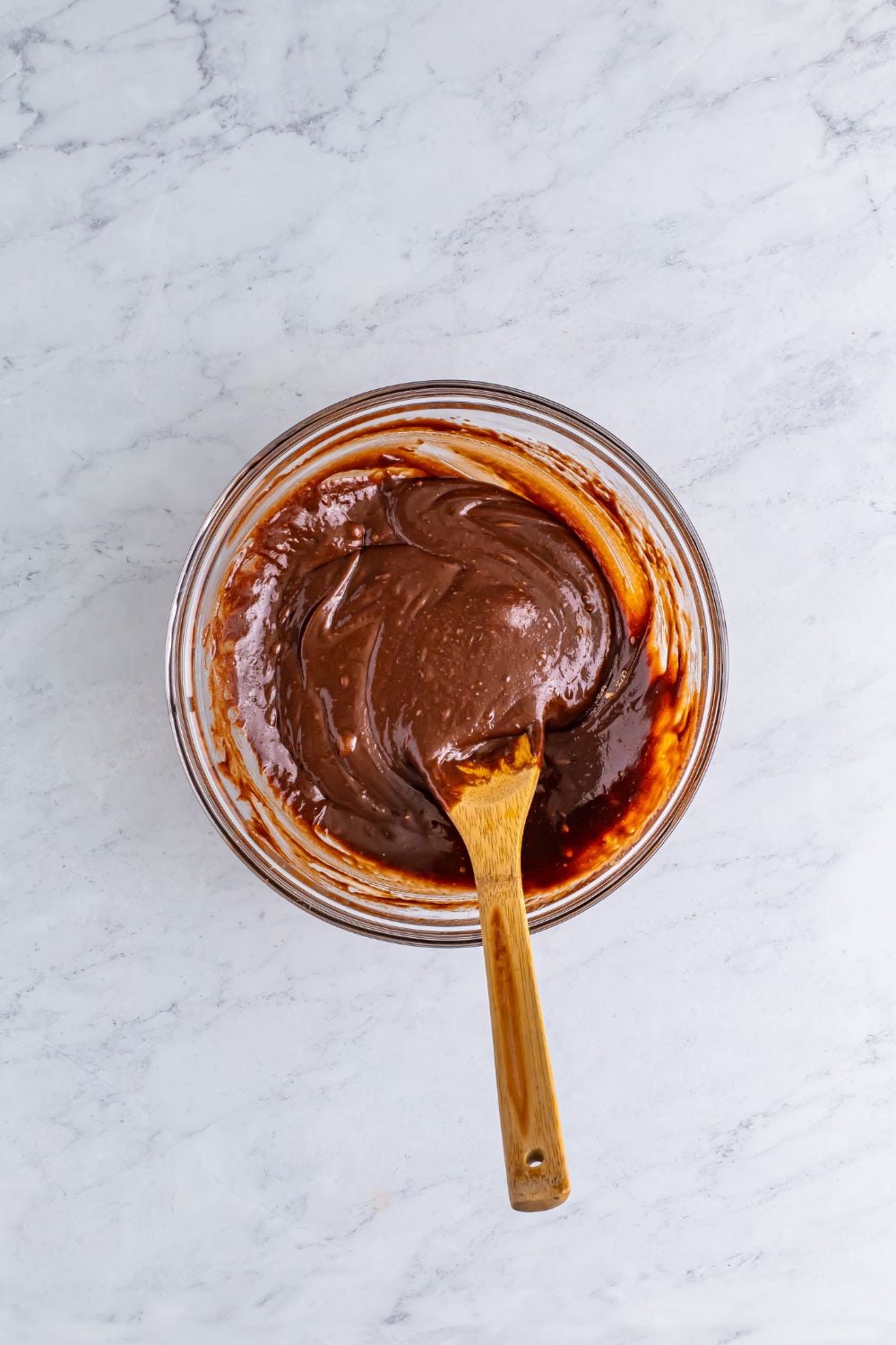 glass bowl of wet brownie batter with a wooden spoon sitting in it