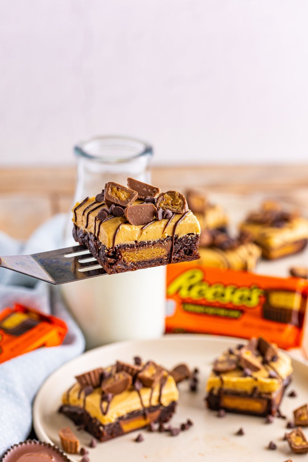 spatula with a peanut butter cup brownie on it above table where more brownies are sliced and plated up