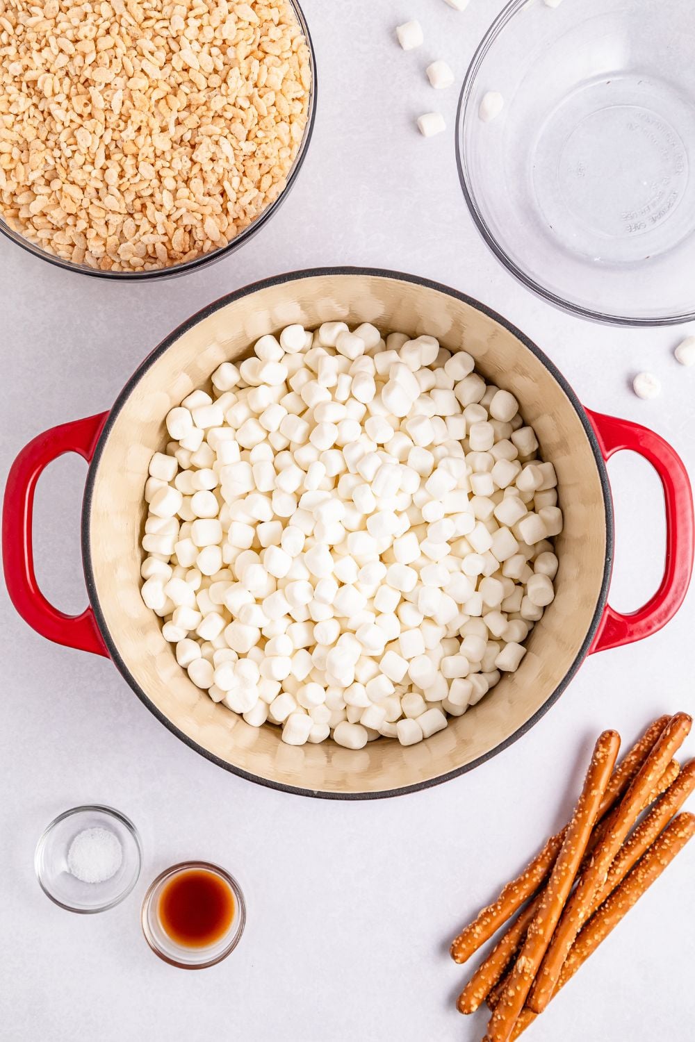 mini marshmallows in a large pot on table with cereal, pretzels and more around it on table