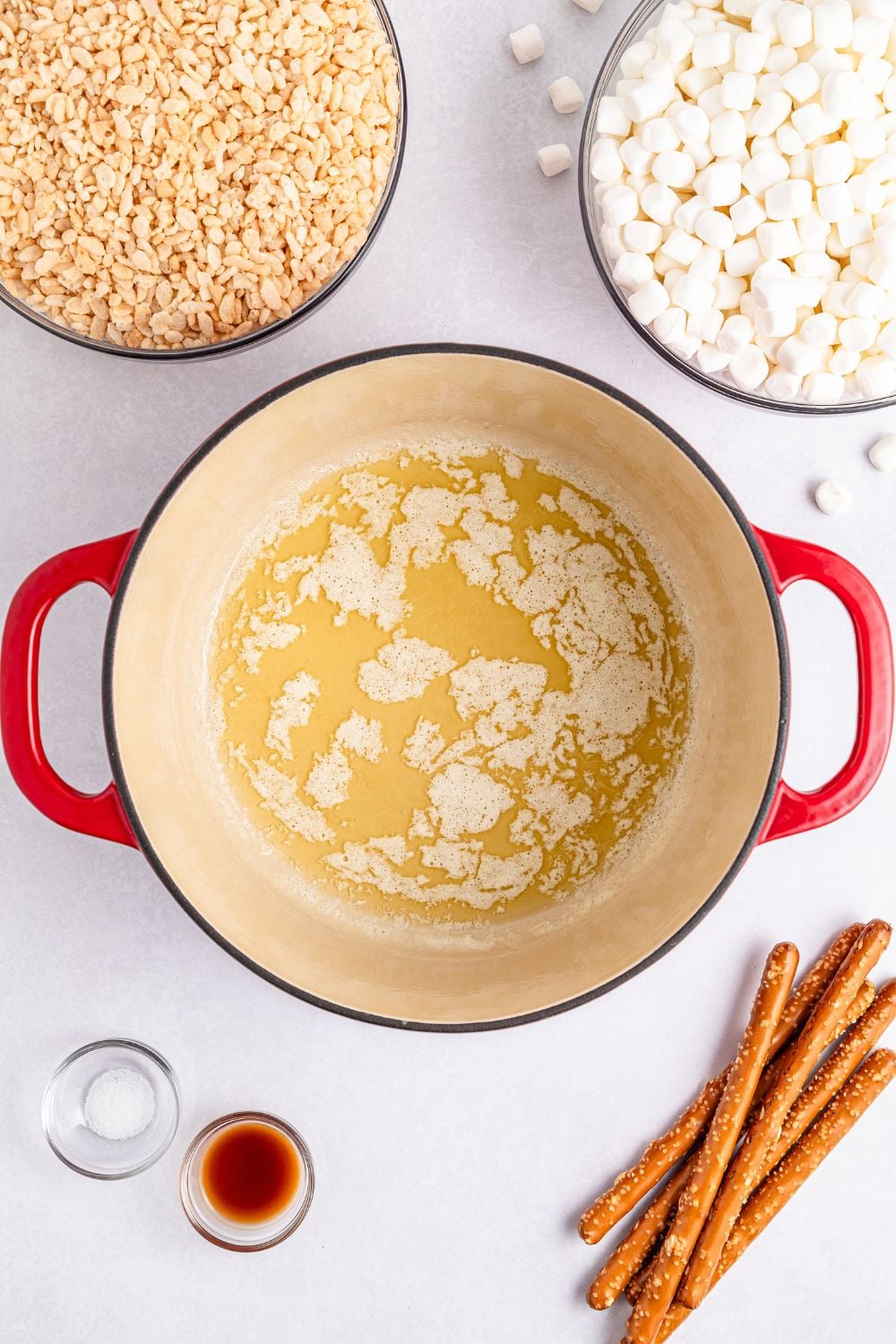 melted butter in a pot with cereal, marshmallows and other ingredients around it on table