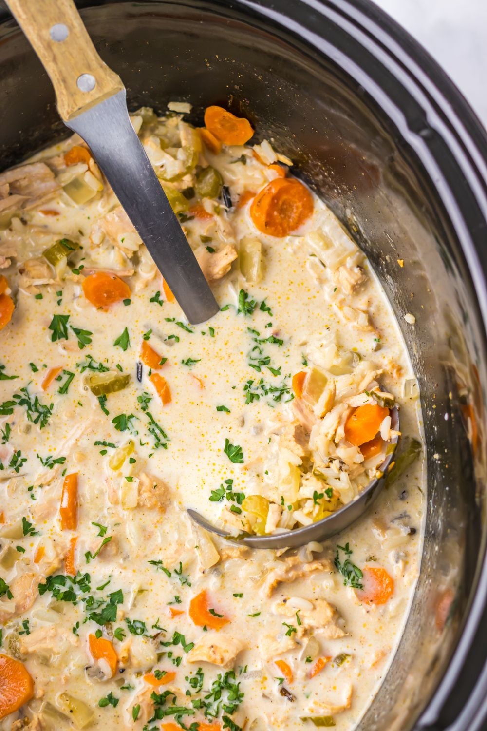 look of slow cooker that is full of a creamy turkey and rice soup that is studded with colorful vegetables