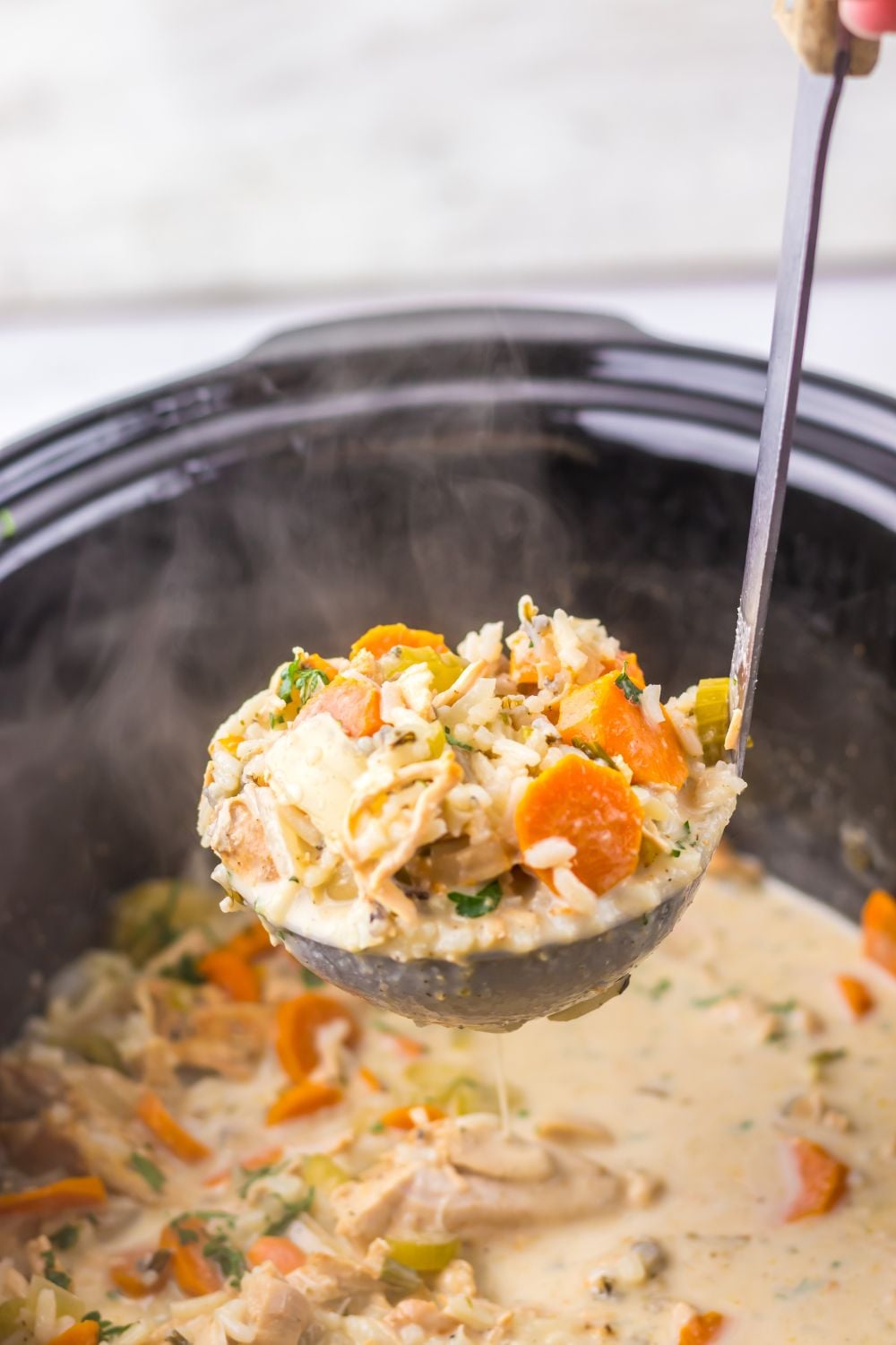 Slow Cooker with Turkey And Rice Soup with a ladle of soup being lifted out of the slow cooker