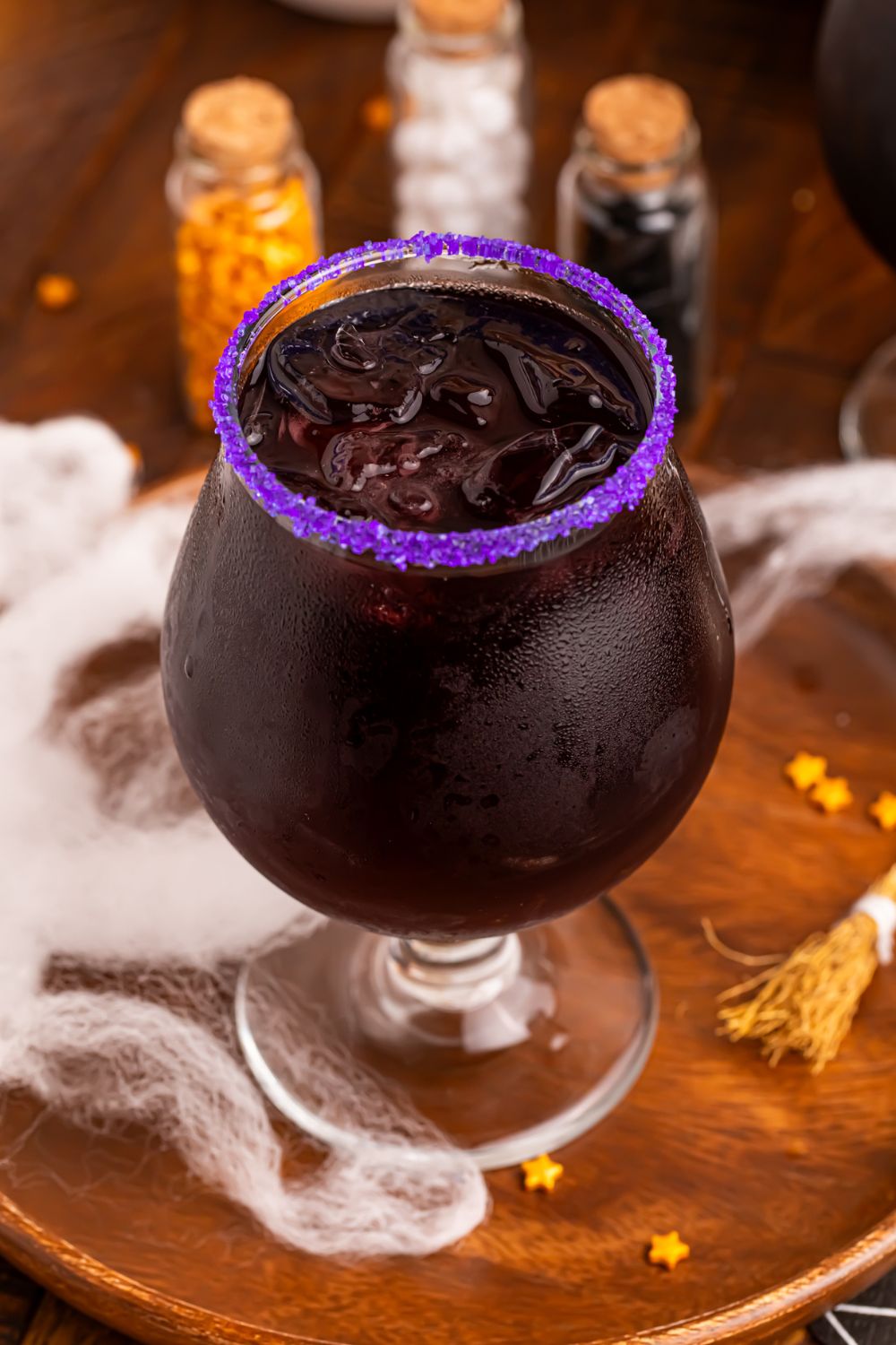 Witches Brew Cocktail on a table with mini bottles of sprinkles in background and fake spiderwebs spread over table for a Halloween vibe