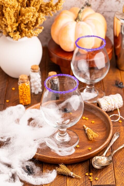 wine glasses sitting on a serving tray with Halloween sprinkles and more around the tray with wine glasses rimmed in sugar