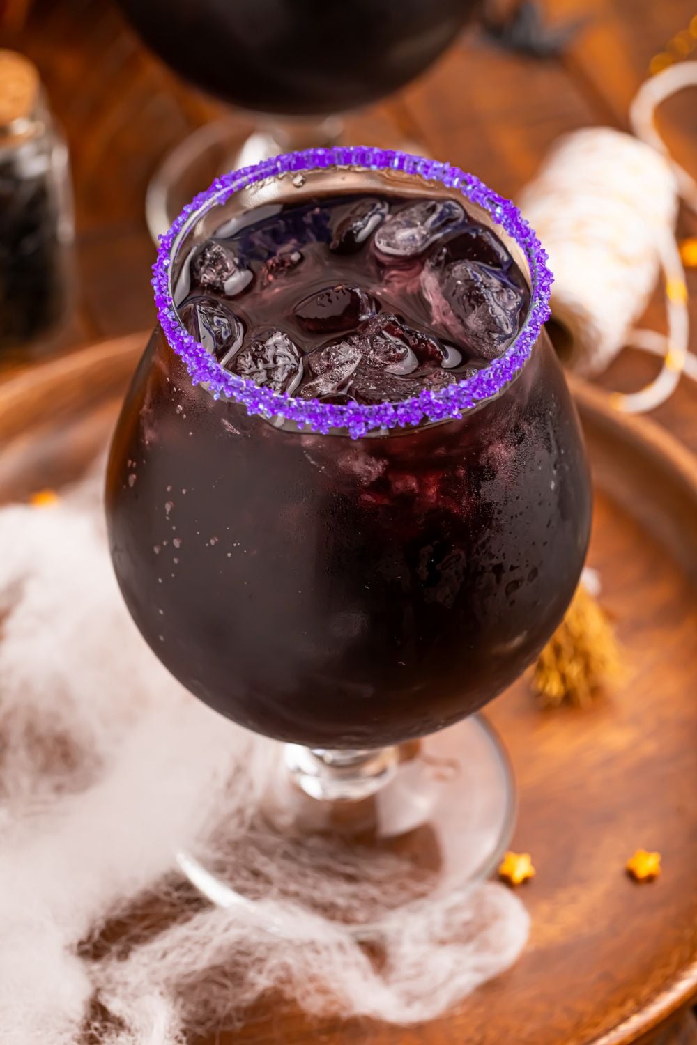 close up of Witches Brew Cocktail in a glass with fake spider web at the bottom of tray with a few candy sprinkles