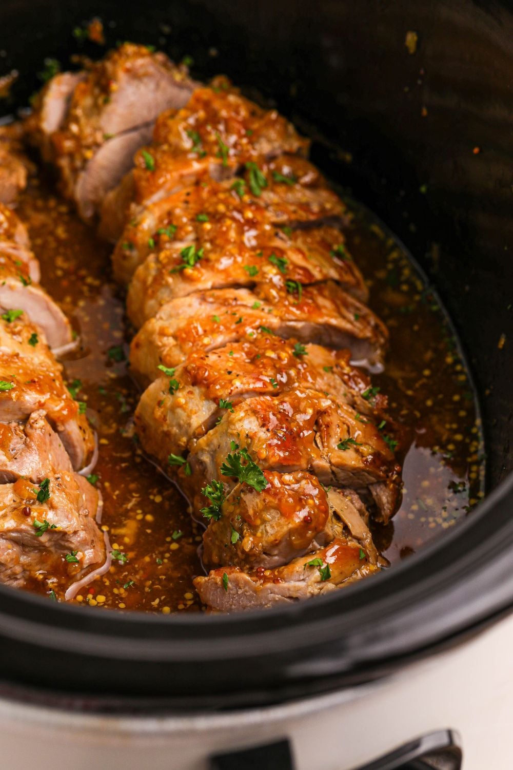 crock pot with a sliced pork tenderloin in a slow cooker