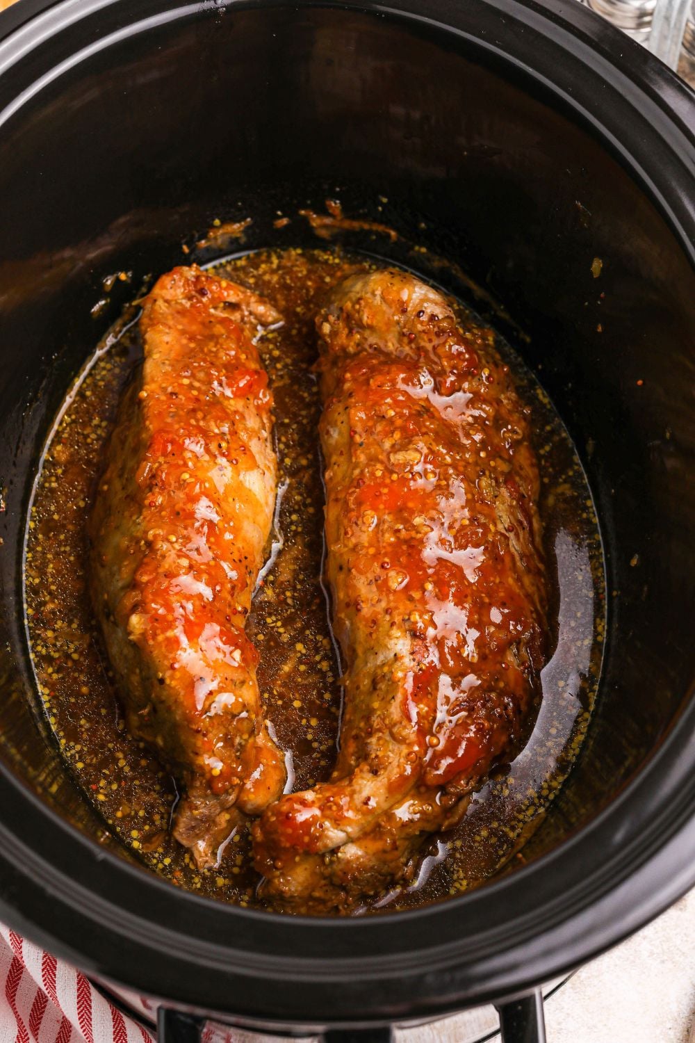 two pork tenderloins in a slow cooker with apricot preserves sauce poured over the meat