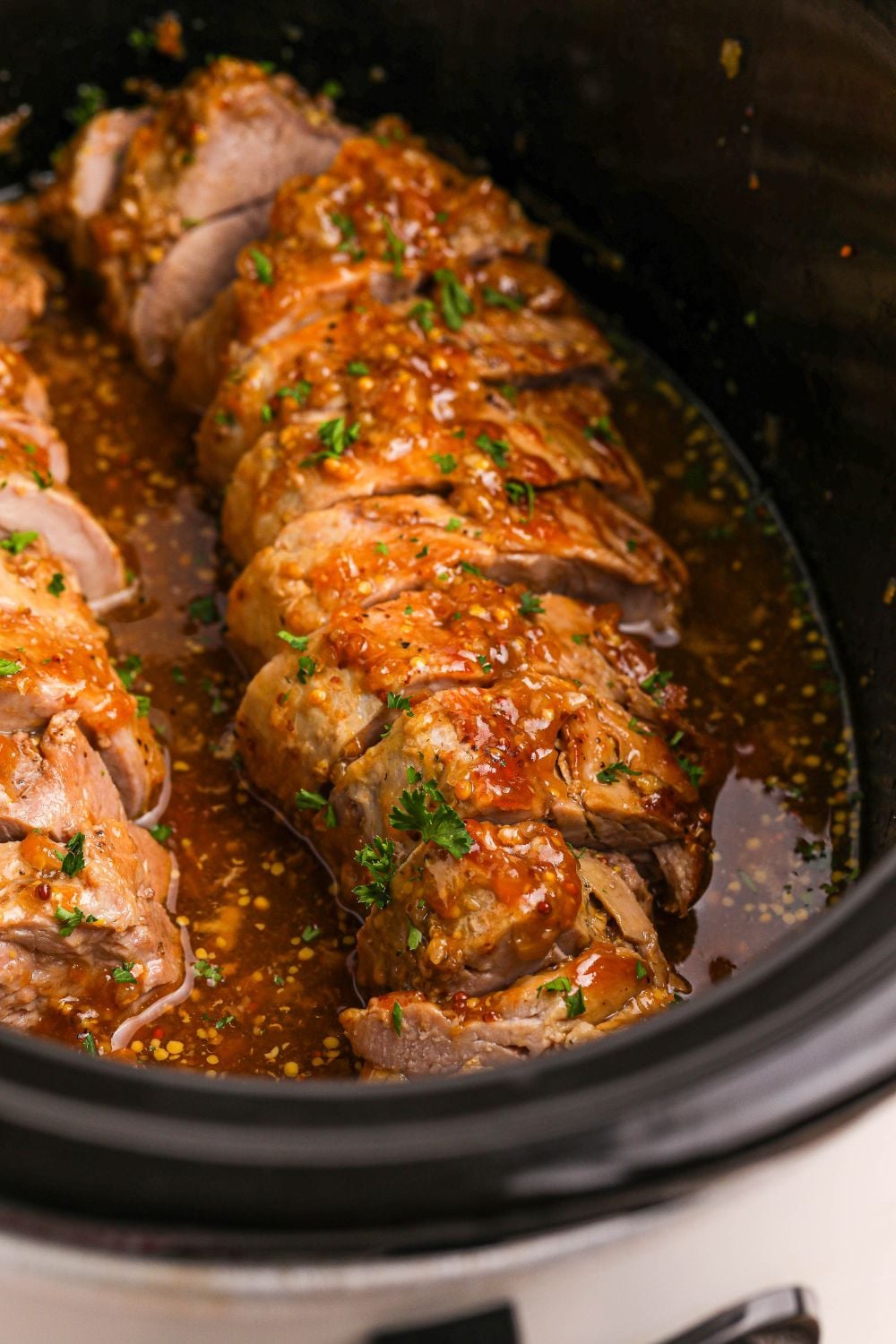 sliced apricot pork in a slow cooker with fresh herbs on top