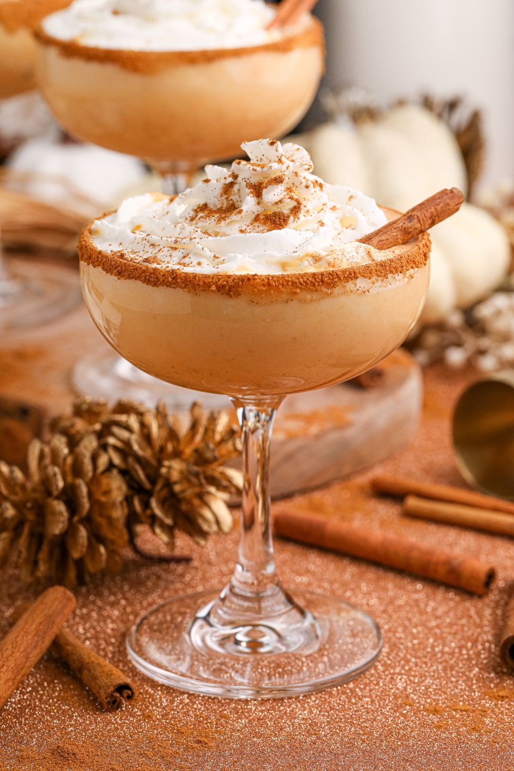 pumpkin spice martinis on table in glasses with pinecones, cinnamon sticks and more spread around the table