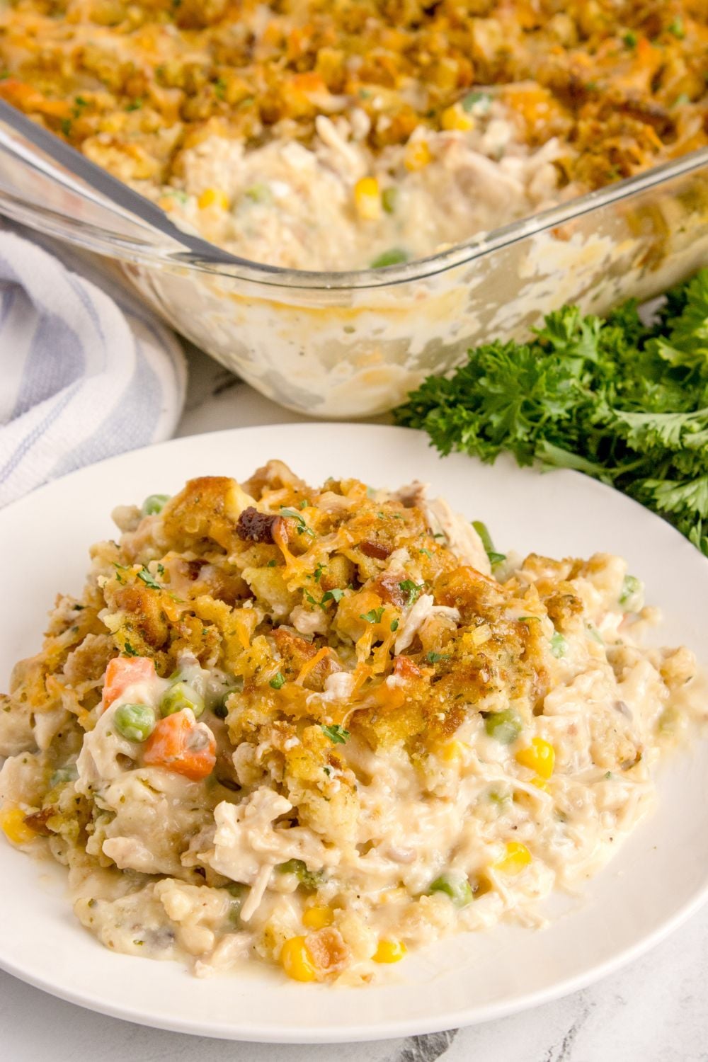 Chicken Stuffing Casserole on a plate with the pan behind it and fresh parsley on the side of pan