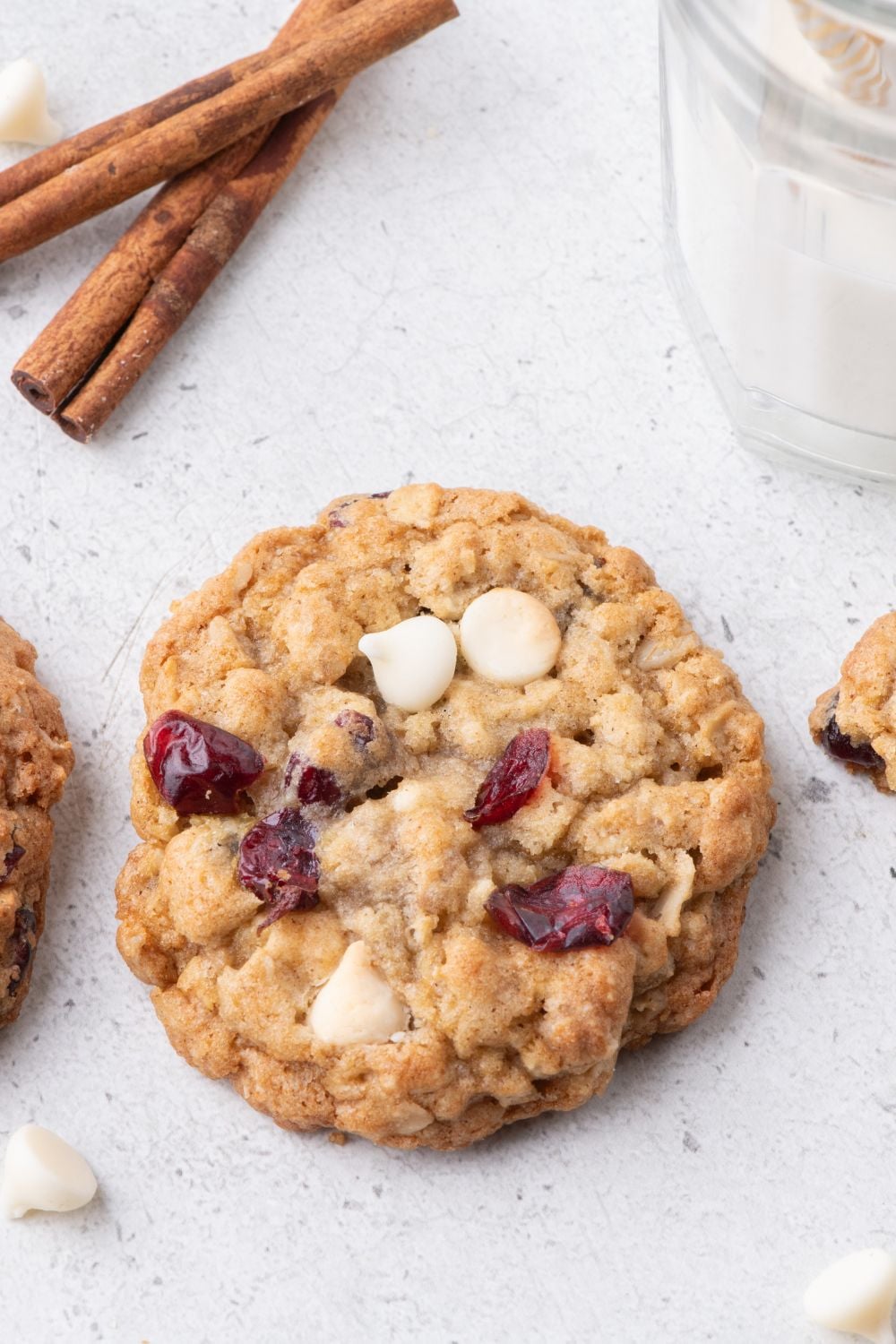 White Chocolate Cranberry Oatmeal Cookies on table with a glass of milk beside the cookie and cinnamon sticks