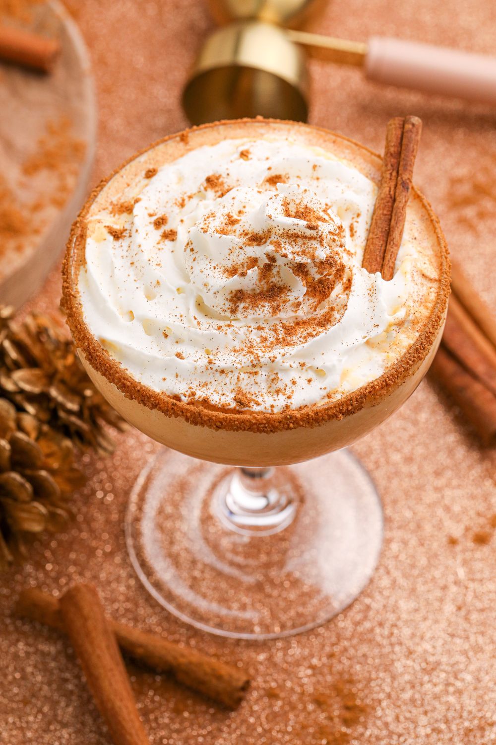 close up of a Pumpkin Pie Martini on table with a cinnamon stick and whipped cream topped on the cocktail with cinnamon sticks on table