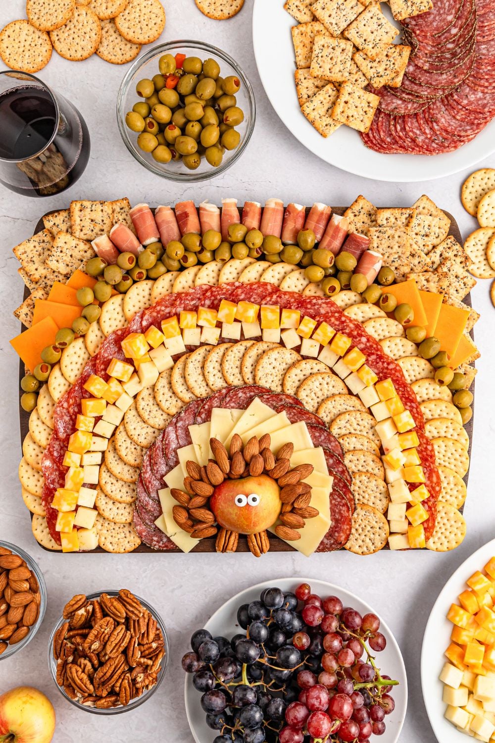 Thanksgiving Turkey Cheese Board on table with bowls of grapes, nuts, platters of meat and cheese surrounding the tray