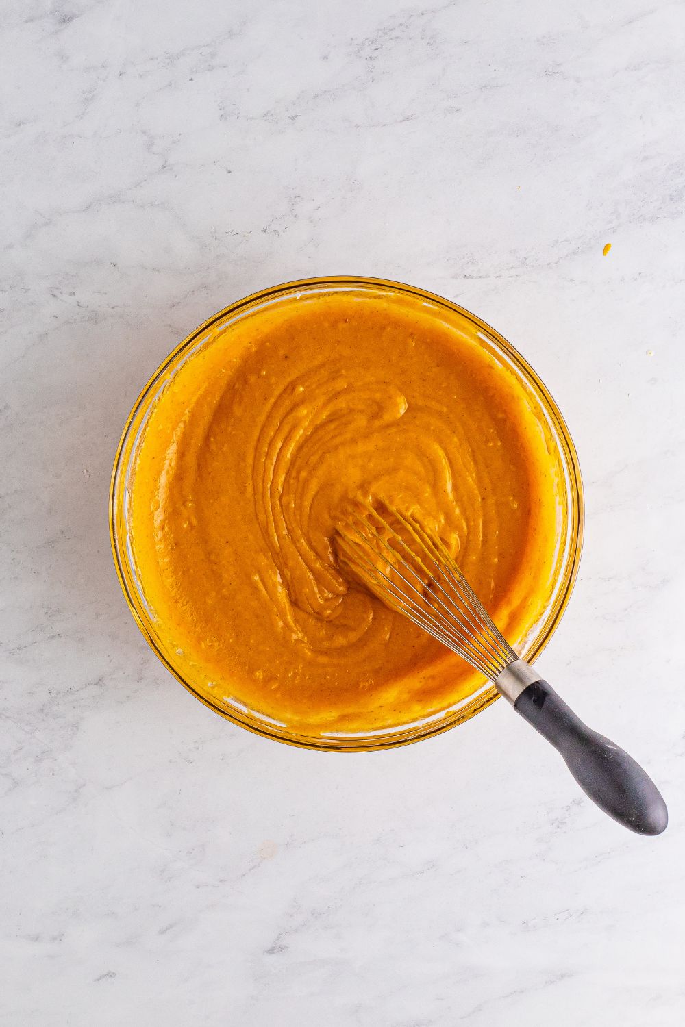 glass bowl with a pumpkin cake batter mixture in it with a whisk