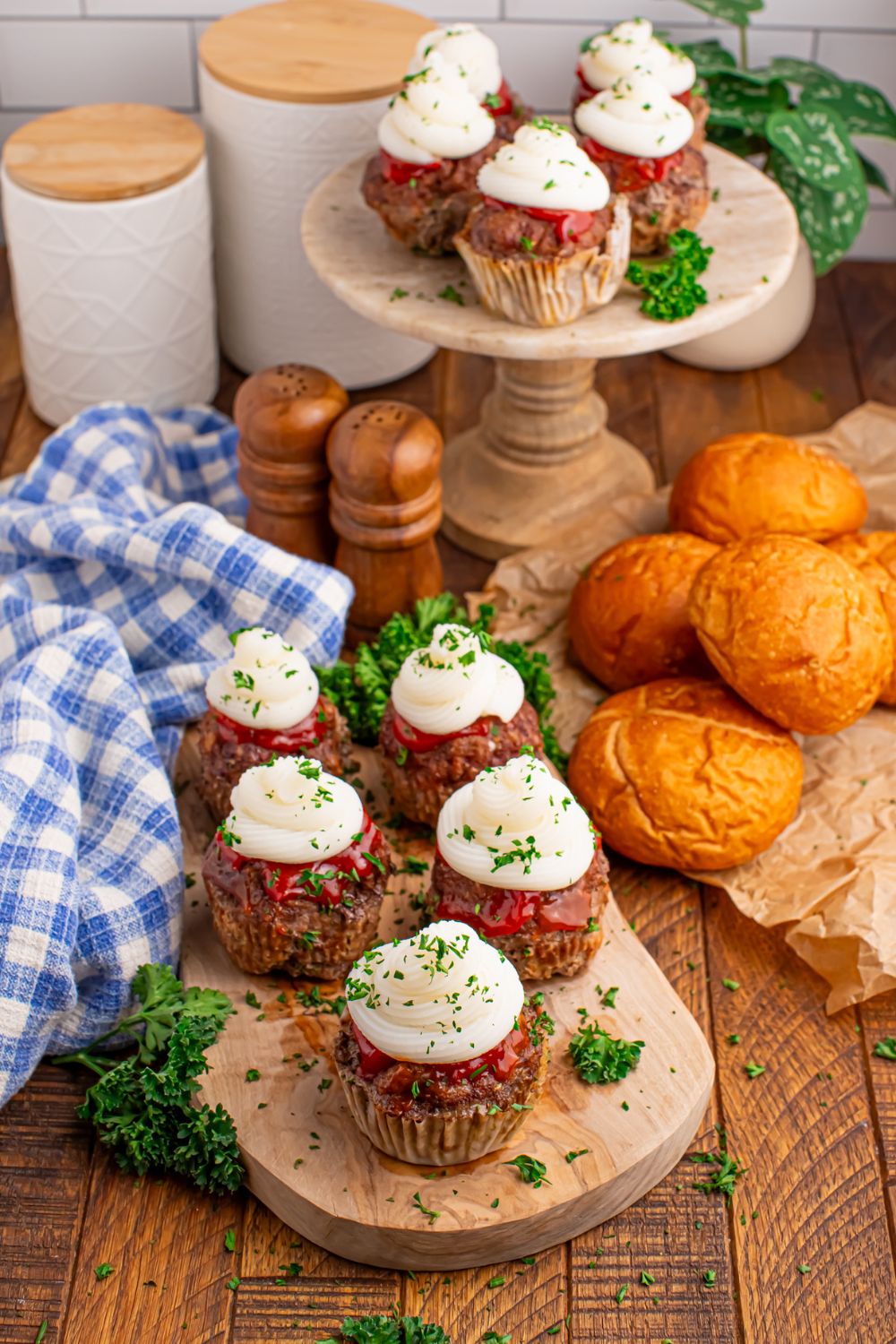 Meatloaf Cupcakes all laid out on trays on table with rolls on the side and towel and containers sitting in the background of picture 