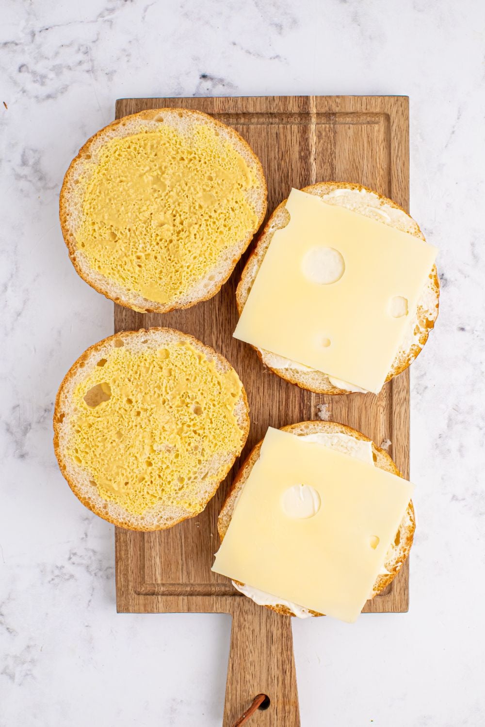 brioche buns sliced in half topped with mayo, mustard and Swiss cheese