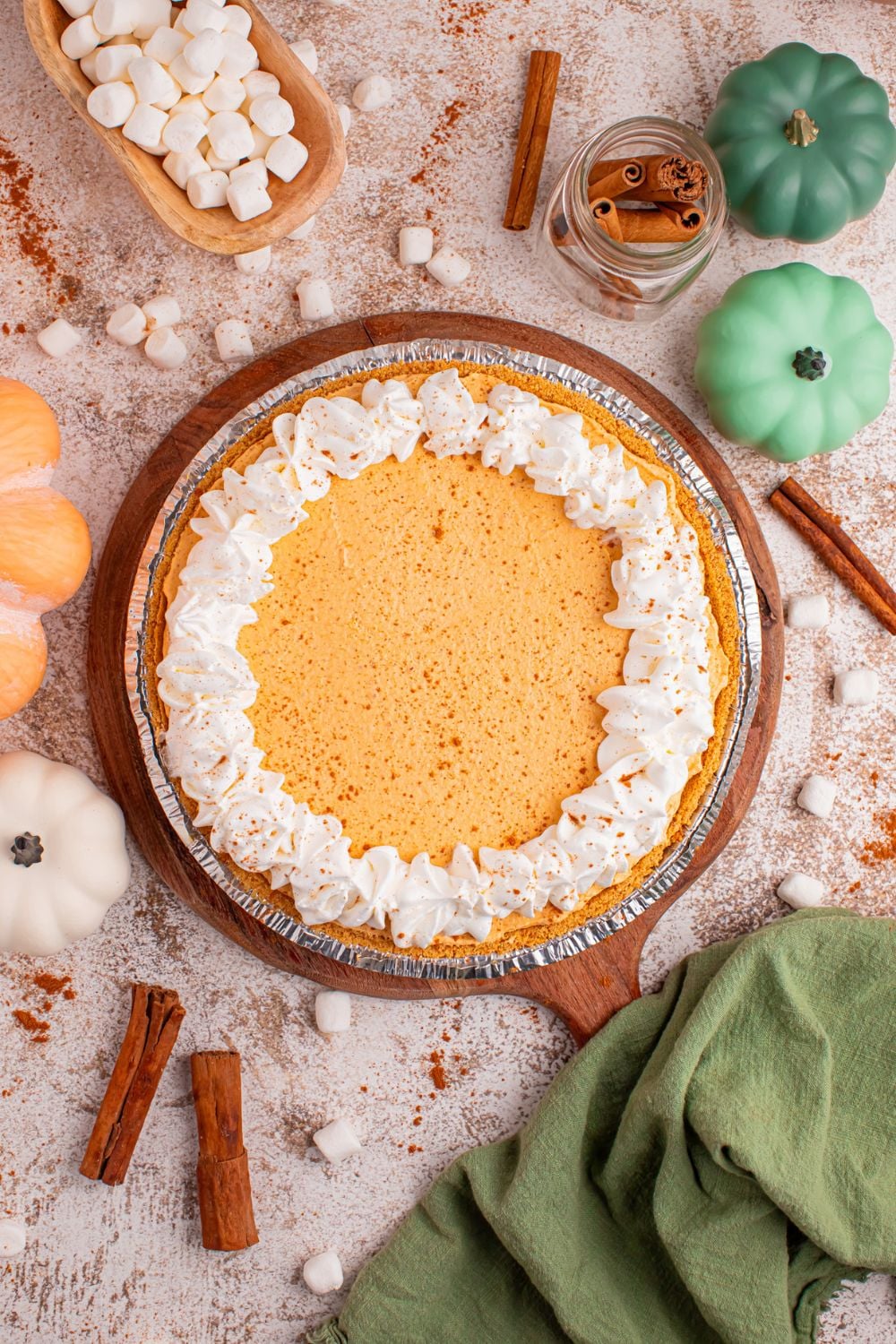 Marshmallow Pumpkin Pie on table with mini marshmallows, fall decor, cinnamon sticks and more around the pie on table