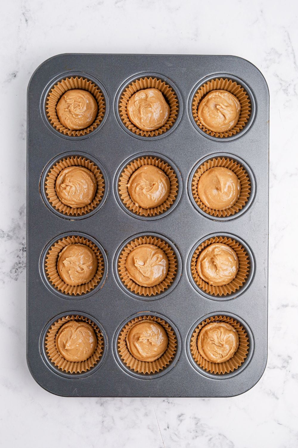 peanut butter poured over chocolate in muffin tin for making Peanut Butter Marshmallow Cups