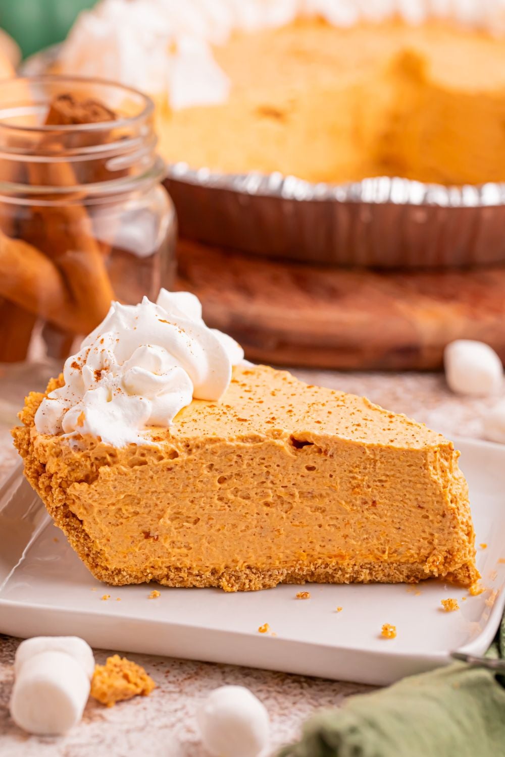 Slice of Marshmallow Pumpkin Pie on plate with the rest of the pie behind it on table