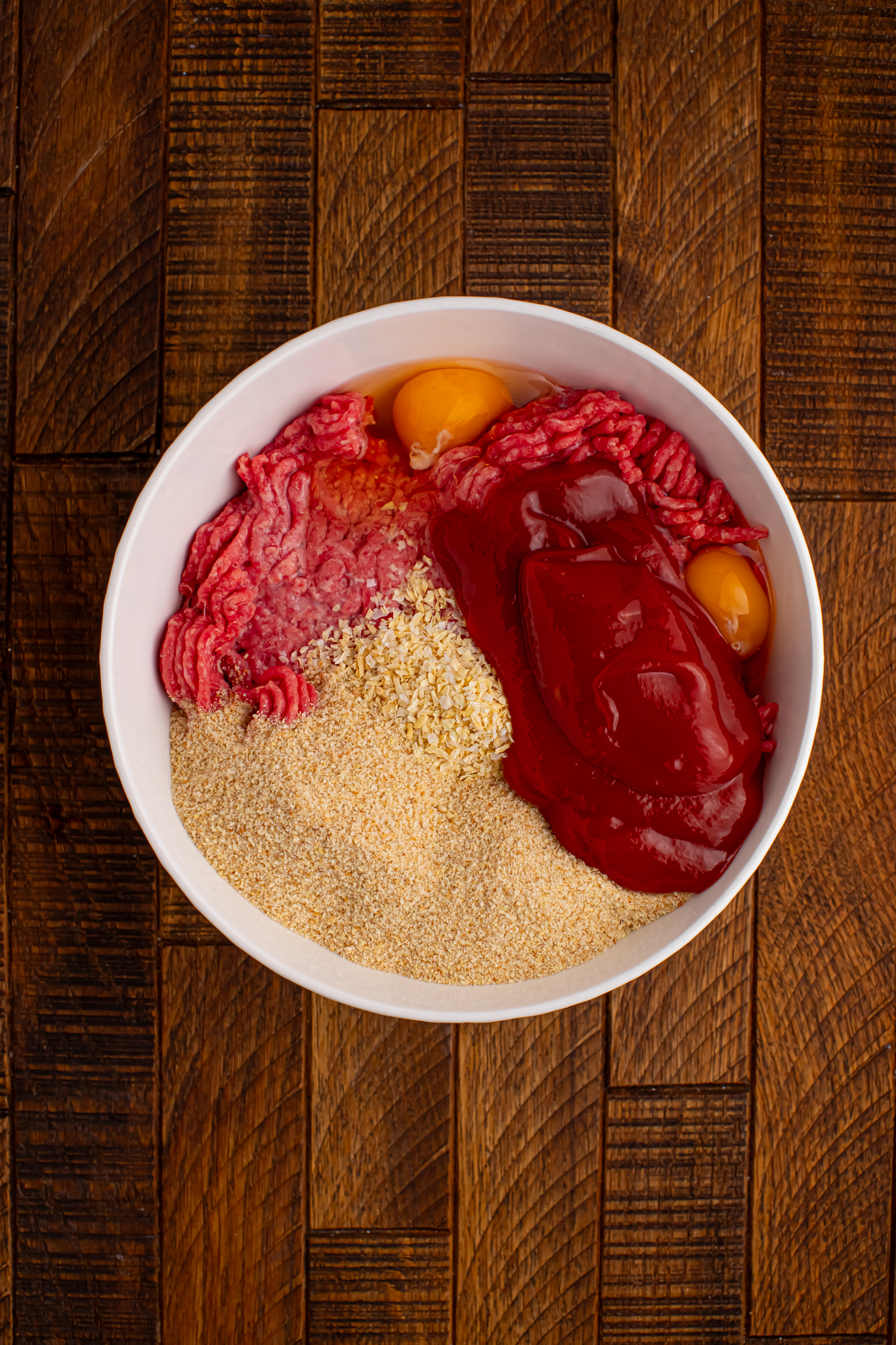 meatloaf ingredients in a white bowl sitting on a wood table 