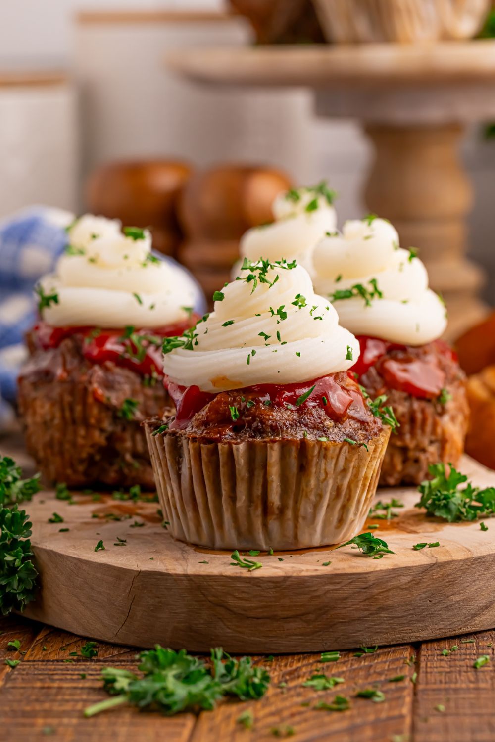 Meatloaf Cupcakes on a wooden cutting board on table with a tray of meatloaf cupcakes in background 