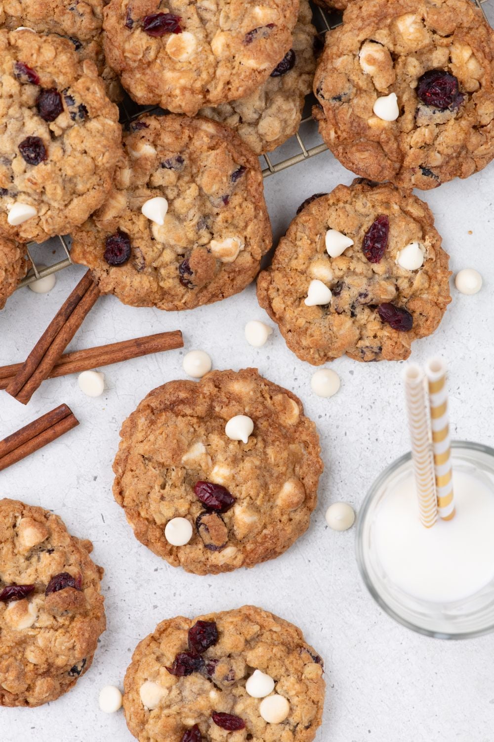 White Chocolate Cranberry Oatmeal Cookies spread out on table with a glass of milk with straws in it