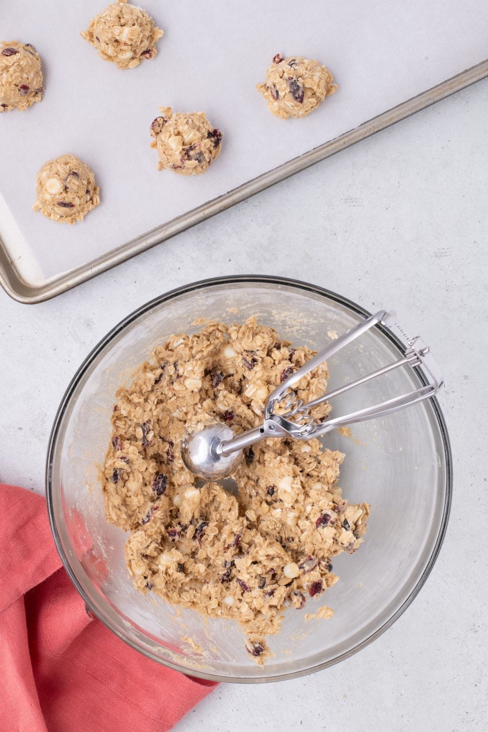 bowl of raw White Chocolate Cranberry Oatmeal Cookie dough on table with baking sheet behind it