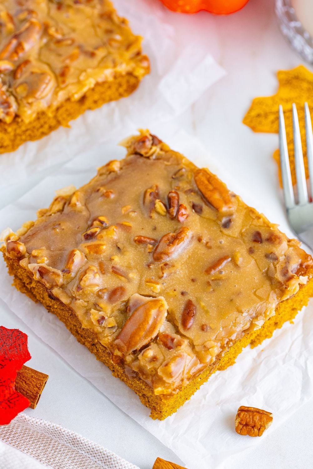 Pumpkin Snack Cake with Praline Icing sliced into squares sitting on table with some nuts and a fork around the slices of cake