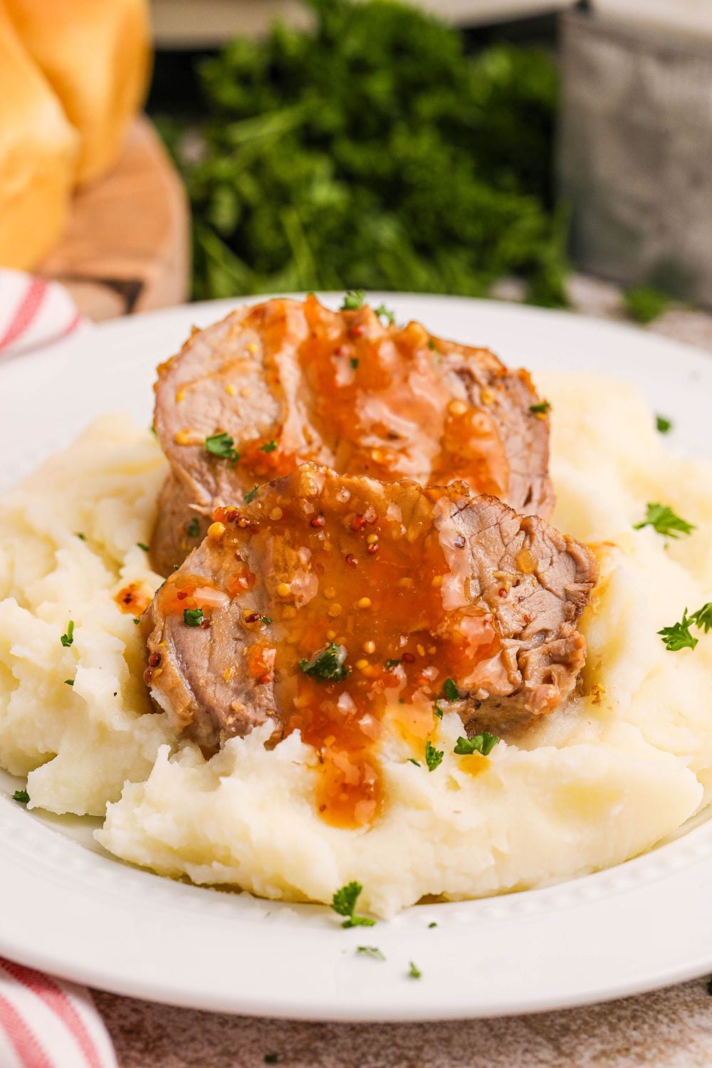 pork tenderloin apricot glaze on top on top of a pile of mashed potatoes on plate on counter