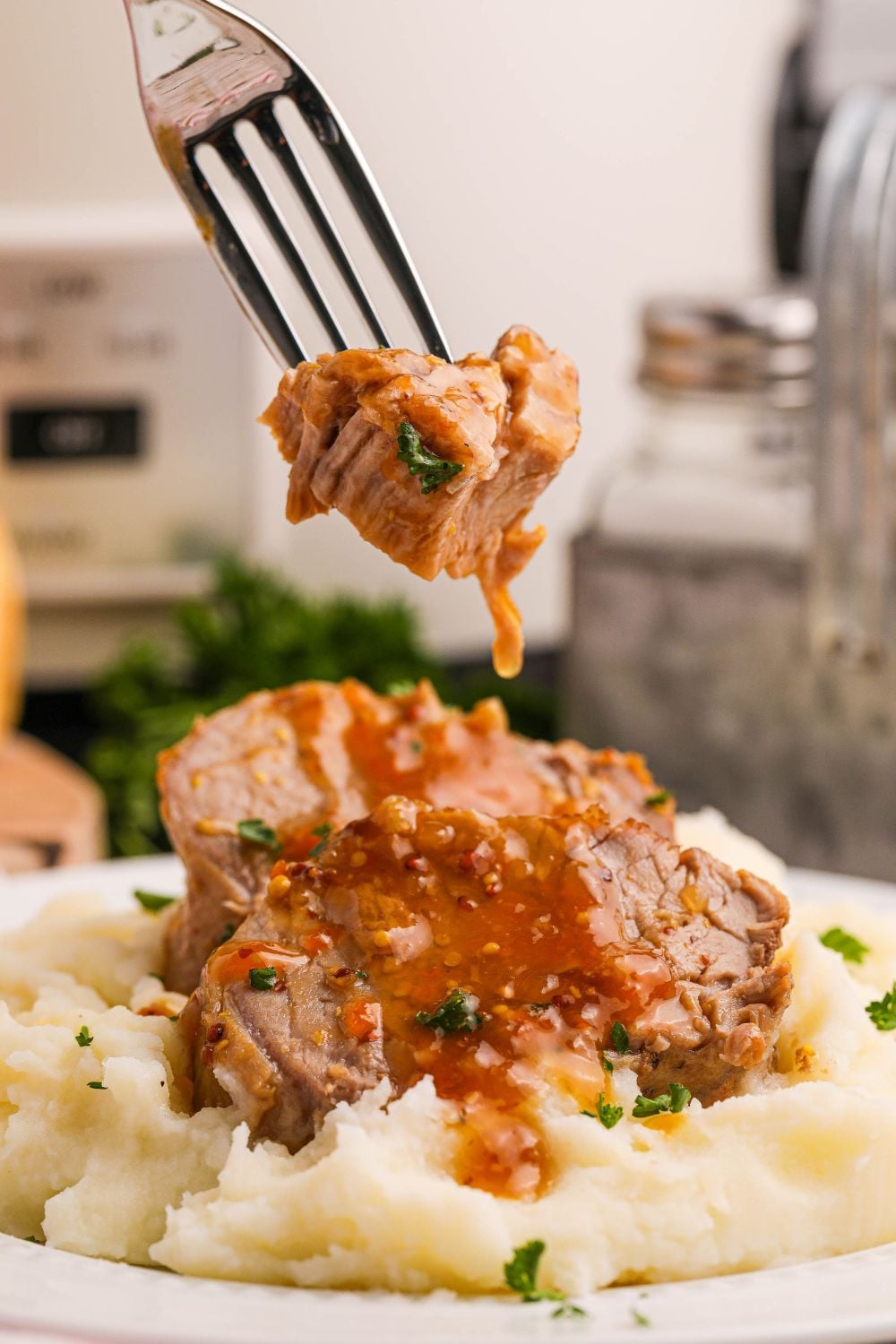 Crock Pot Apricot Pork Tenderloin sliced and placed on a plate with mashed potatoes and a fork with a bite of pork on it