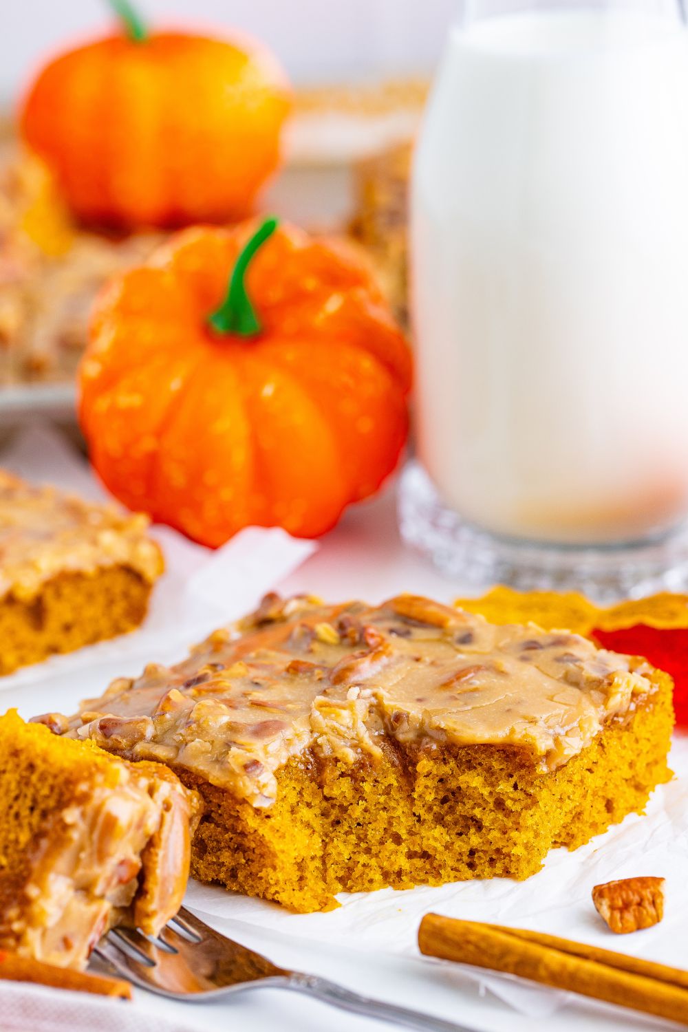 slice of cake on plate with a fork full to the side and a cinnamon stick sitting on table of the pumpkin snack cake