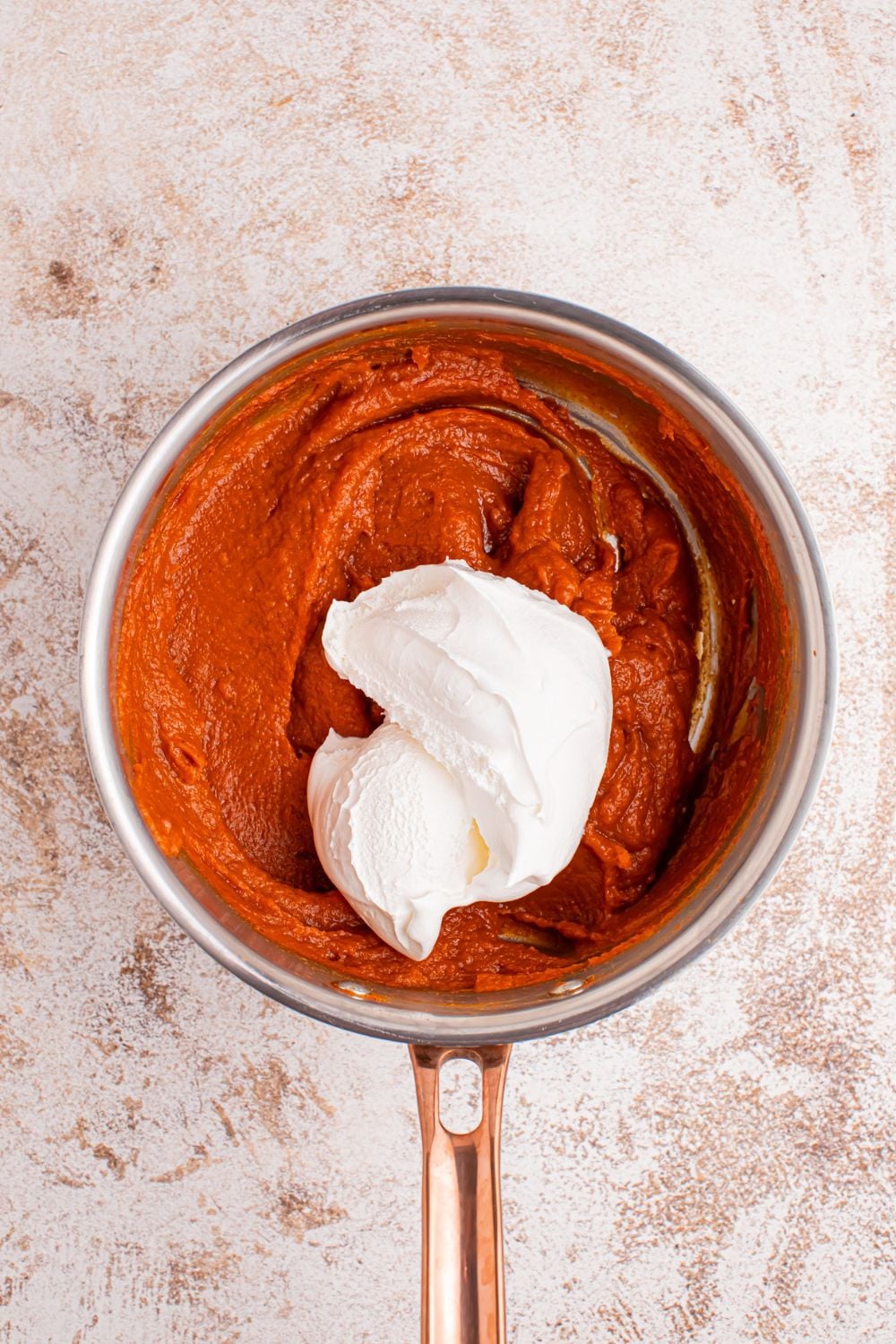 Marshmallow Pumpkin Pie batter in a saucepan with Cool Whip dollop on top of pumpkin mixture