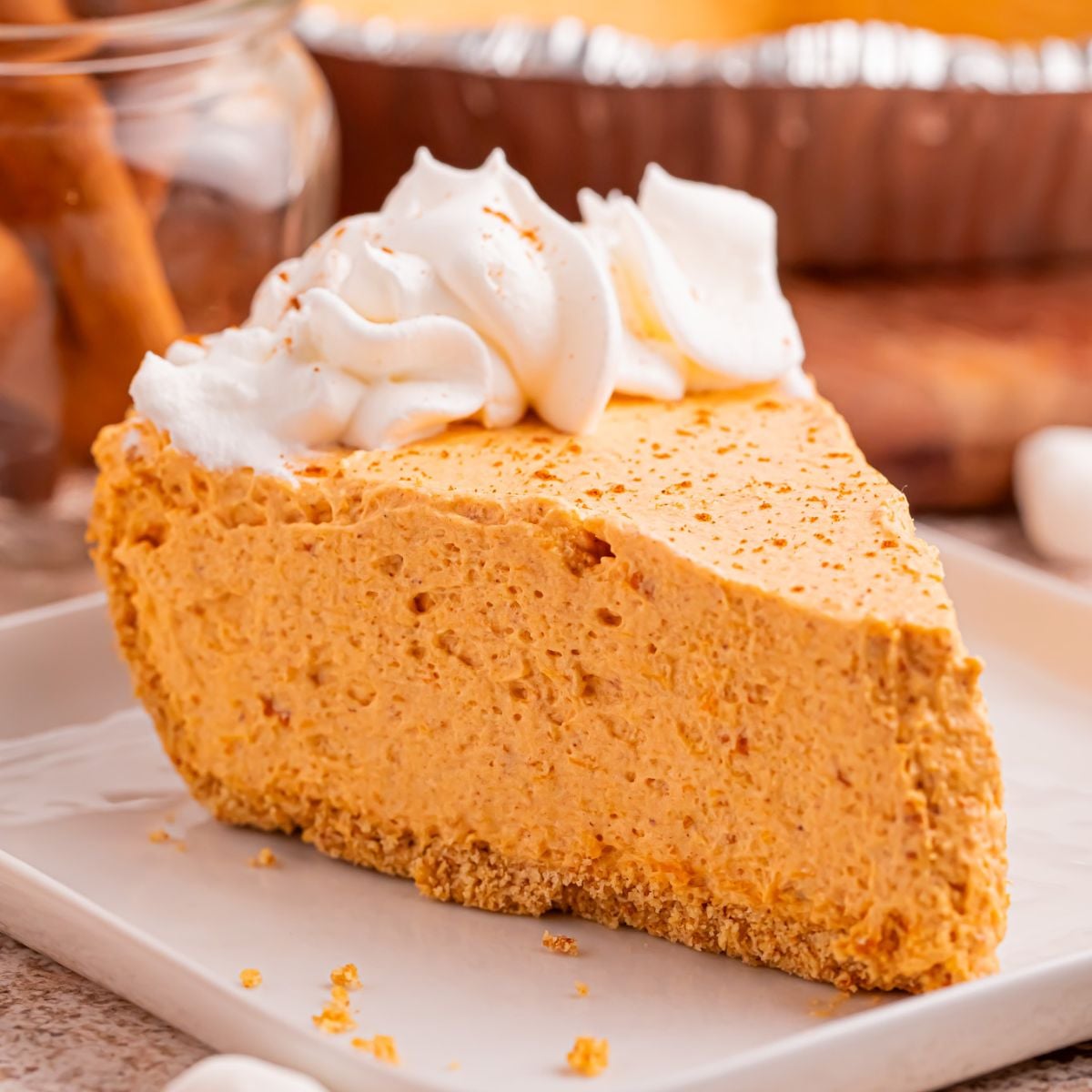 Slice of Marshmallow Pumpkin Pie on plate with a few crumbs from crust sprinkled on around the table