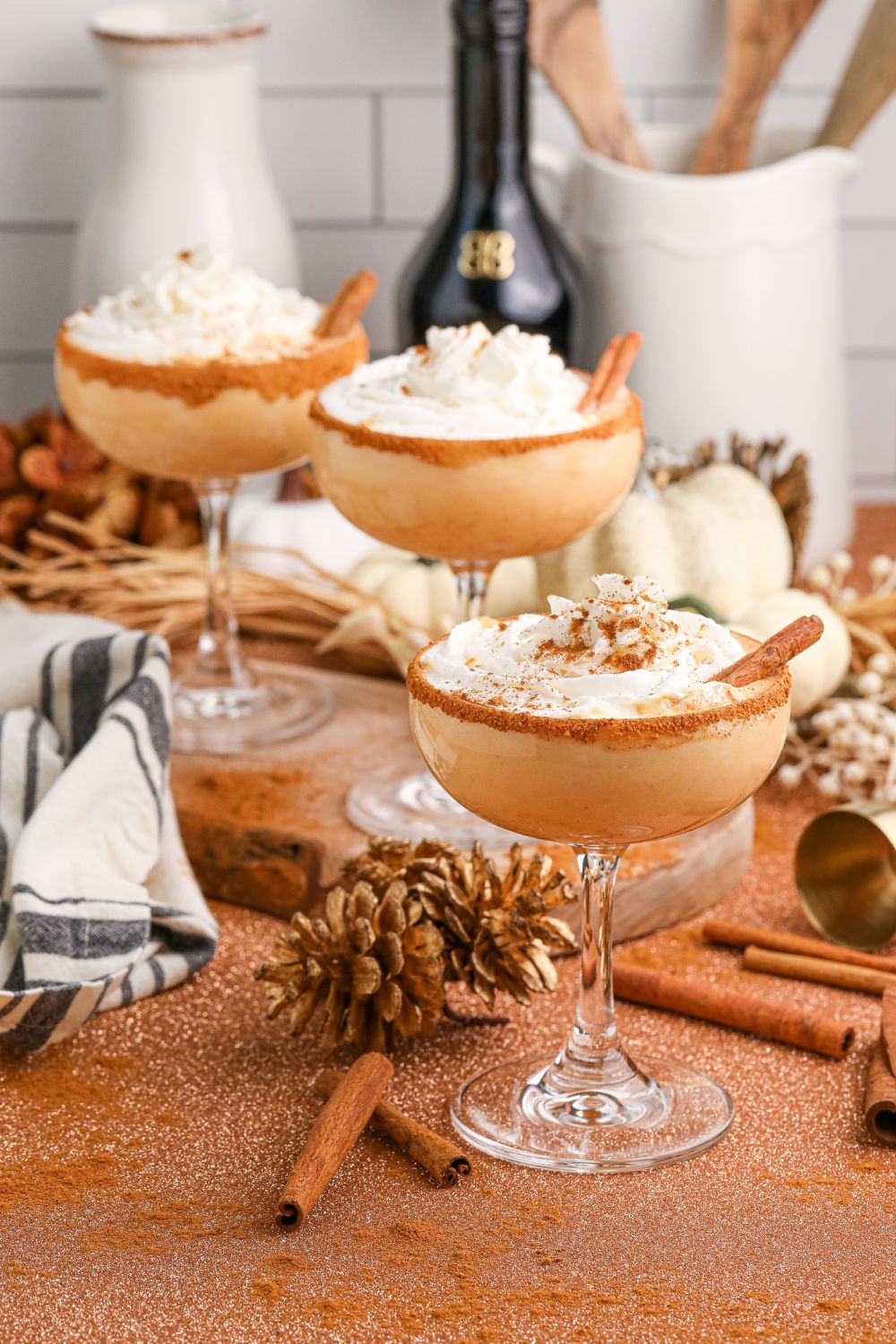 glasses of pumpkin martinis on table with bottles of alcohol to show ingredients in it in the background and fall decor on table
