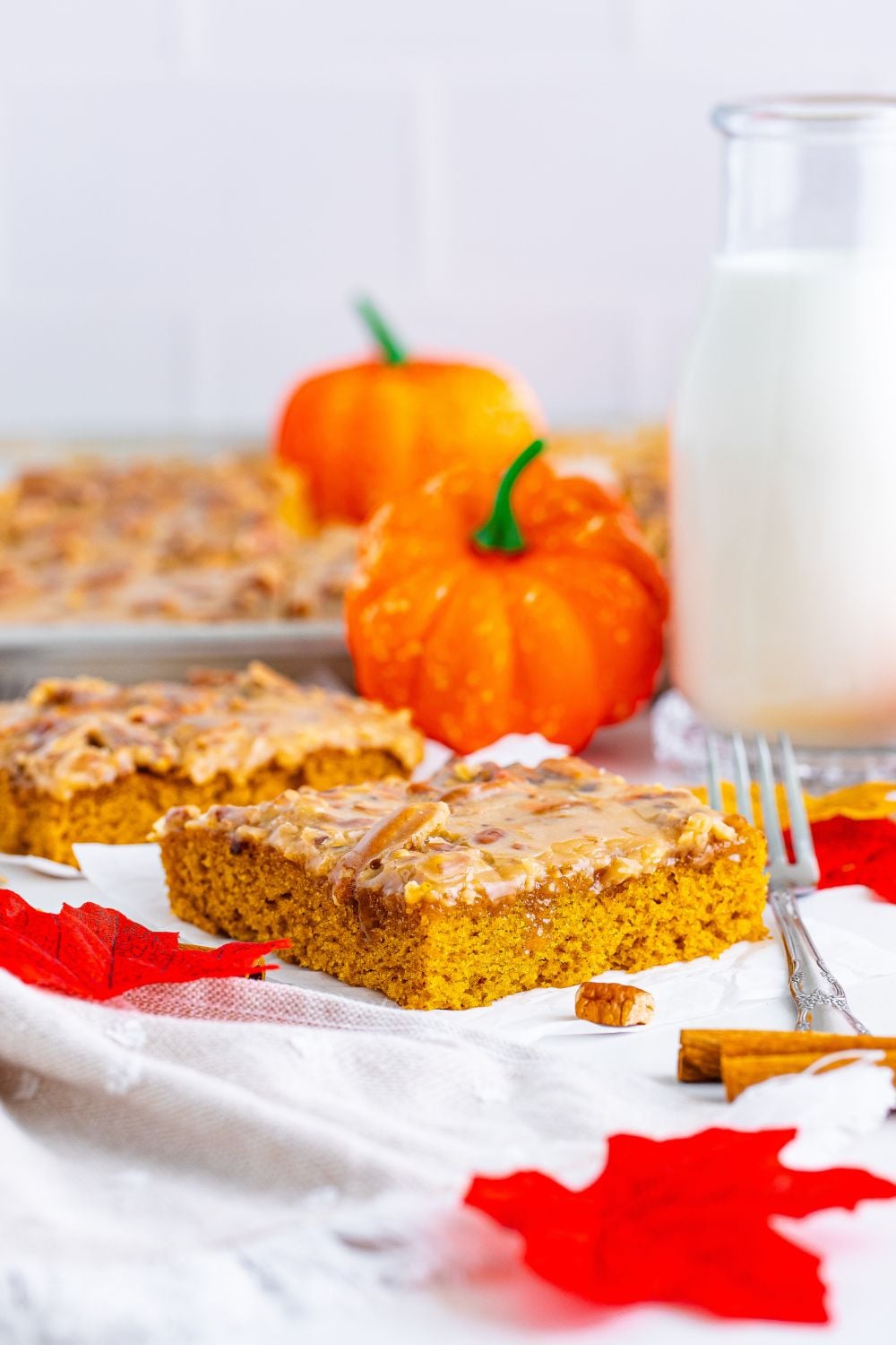 Pumpkin Snack Cake with Praline Icing sliced and placed on table with a glass of milk to side and pan of cake sitting behind it