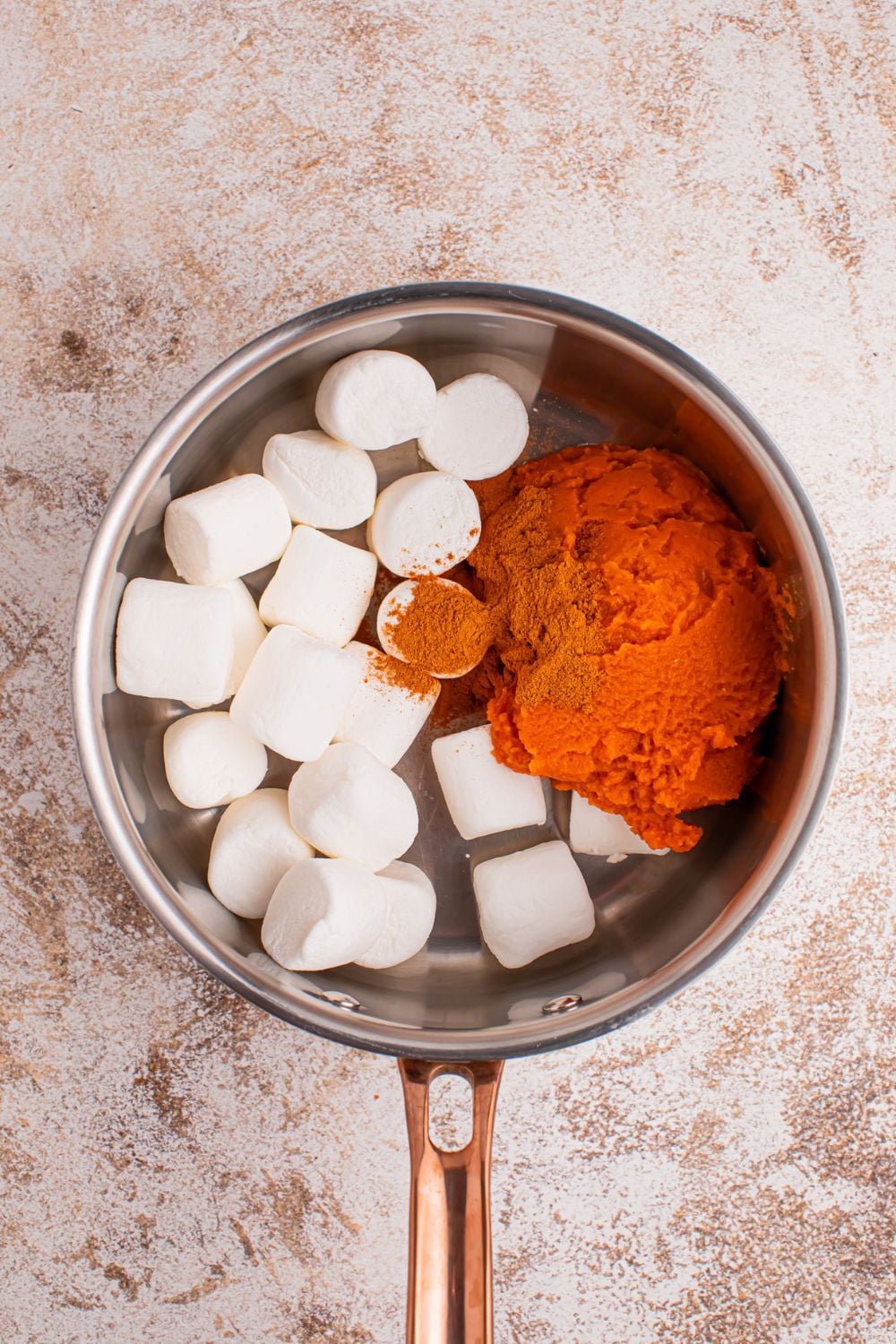 large marshmallows, pumpkin spice and pumpkin puree in a sauce pan sitting on table