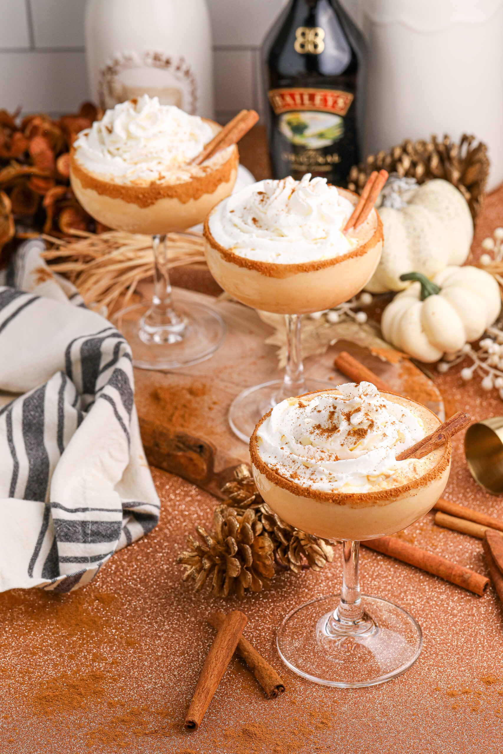 glasses of pumpkin martinis on table with bottles of alcohol to show ingredients in it in the background and fall decor on table