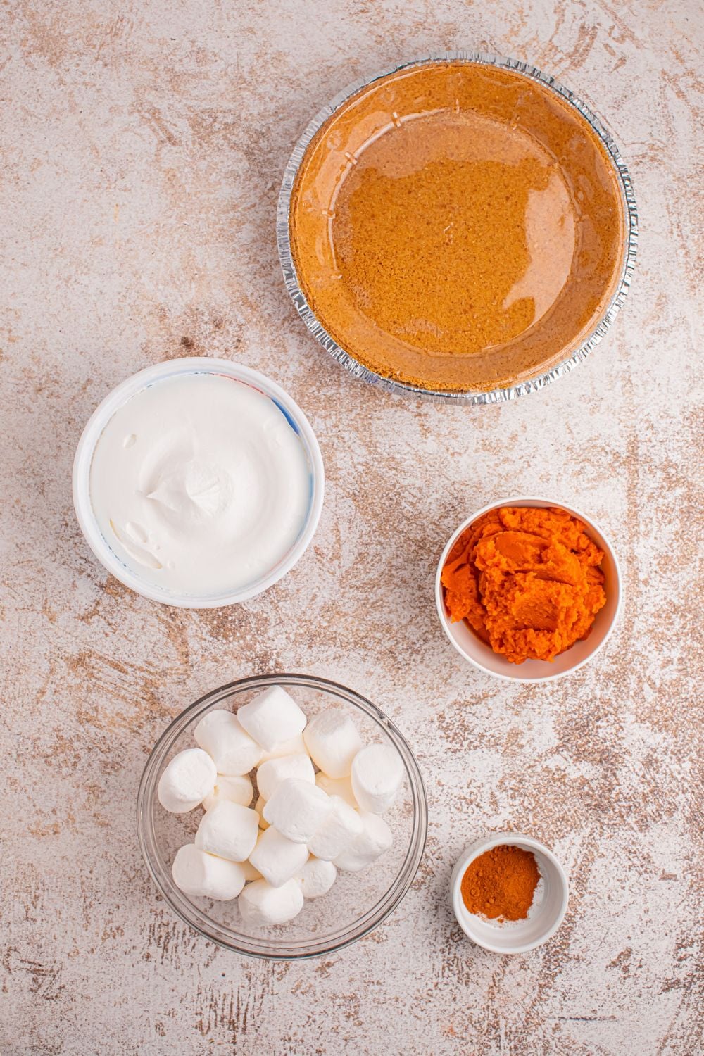 ingredients for a pumpkin marshmallow pie in single serve bowls sitting on a table