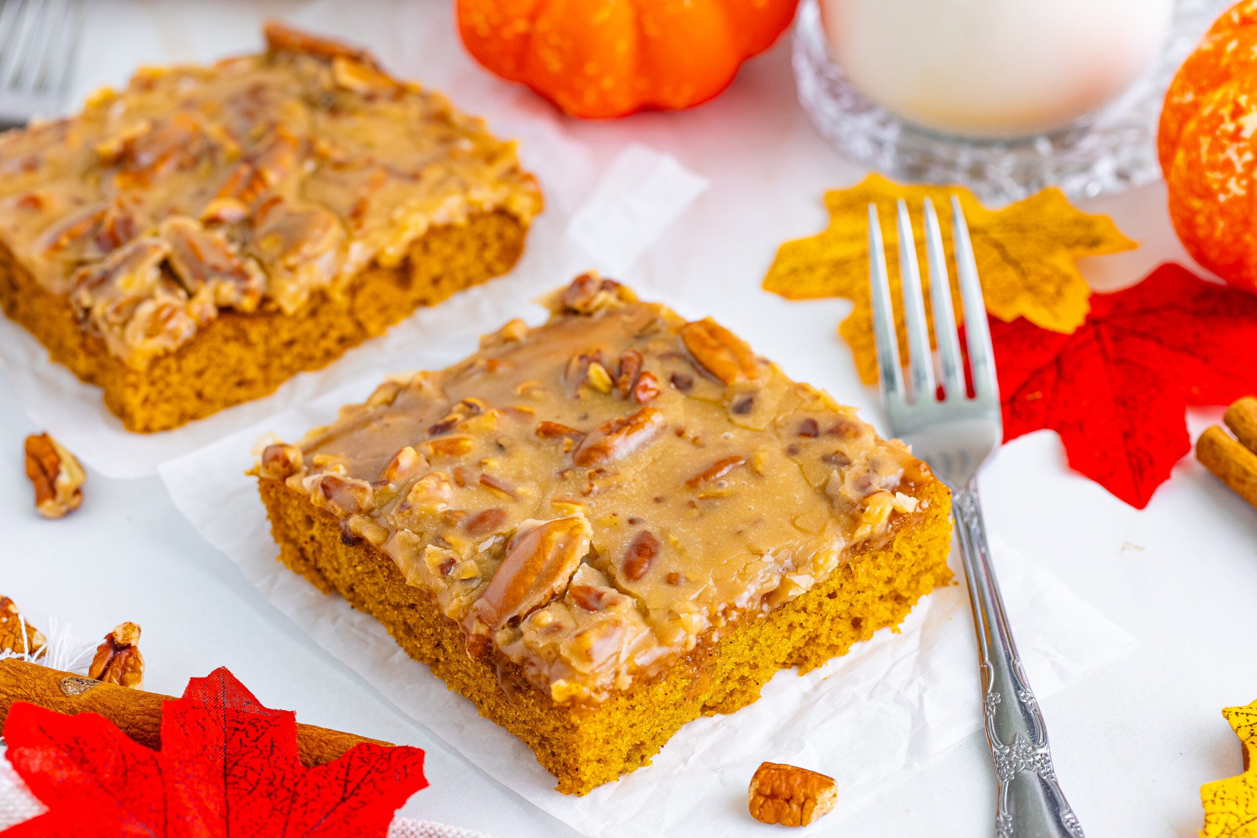 Pumpkin Snack Cake with Praline Icing slices on a white table surrounded by fall leaves