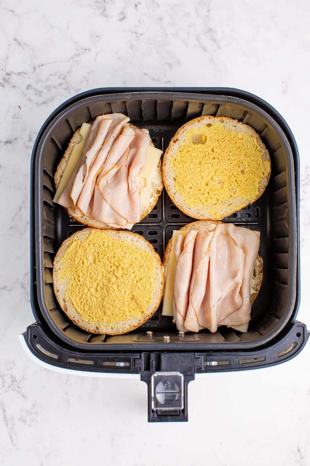air fryer with turkey sandwiches open faced inside the basket 