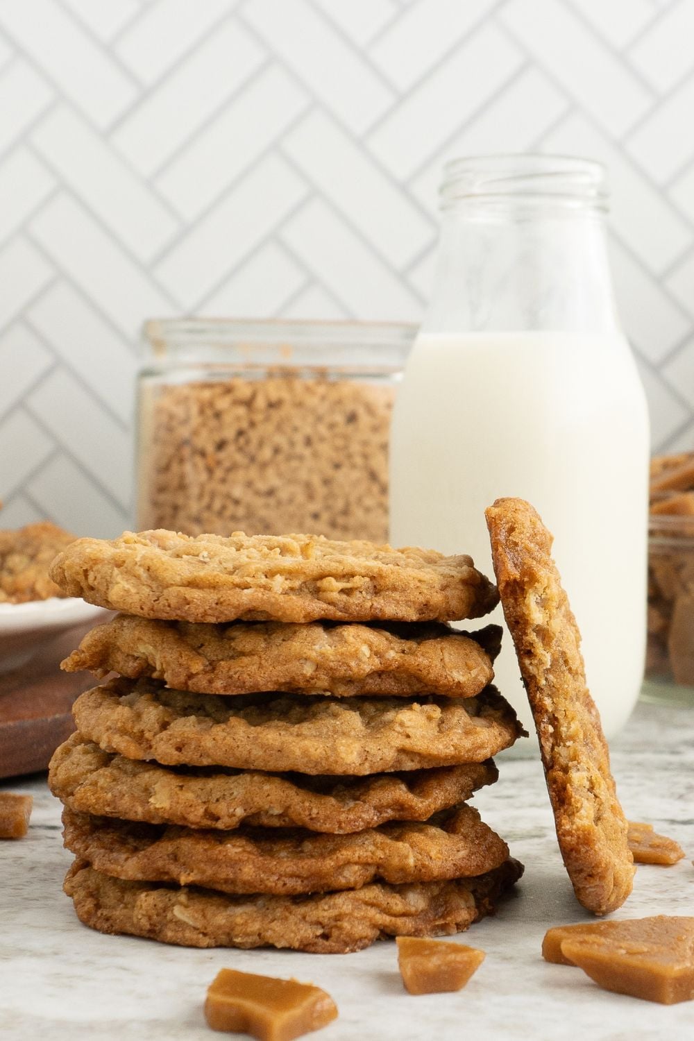 Oatmeal Toffee Cookies stacked up on top of each other, with a glass of milk behind it 