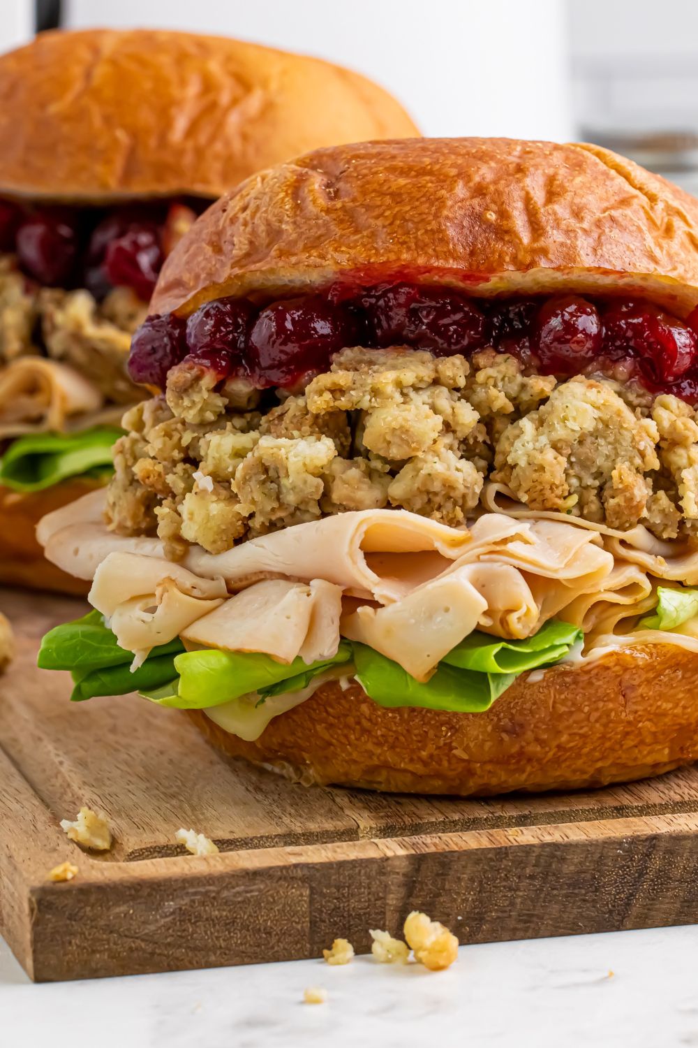 Leftover Turkey Sandwich on table with a close up of the meat, lettuce, stuffing and cranberry sauce on the bun 