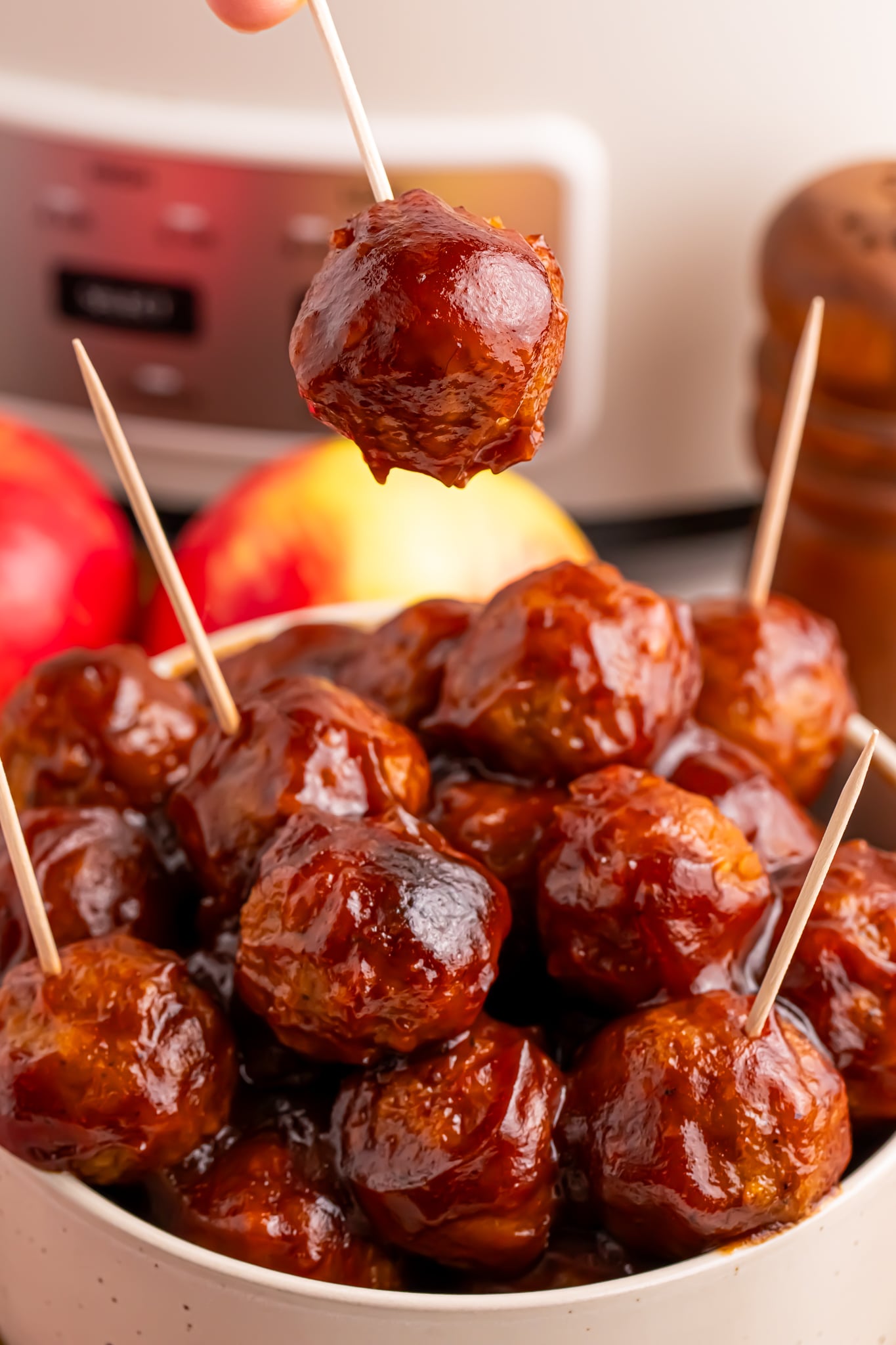 bowl of meatballs with toothpicks in it, and one being lifted out of the bowl on by a hand