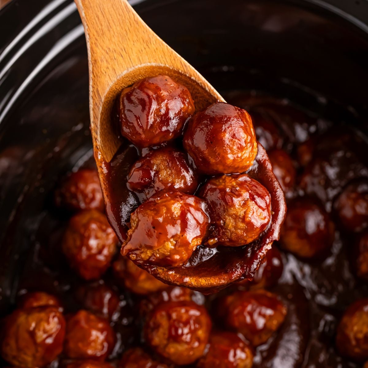 Crockpot Apple Butter Meatballs in crockpot on counter with wooden spoon with some meatballs in it