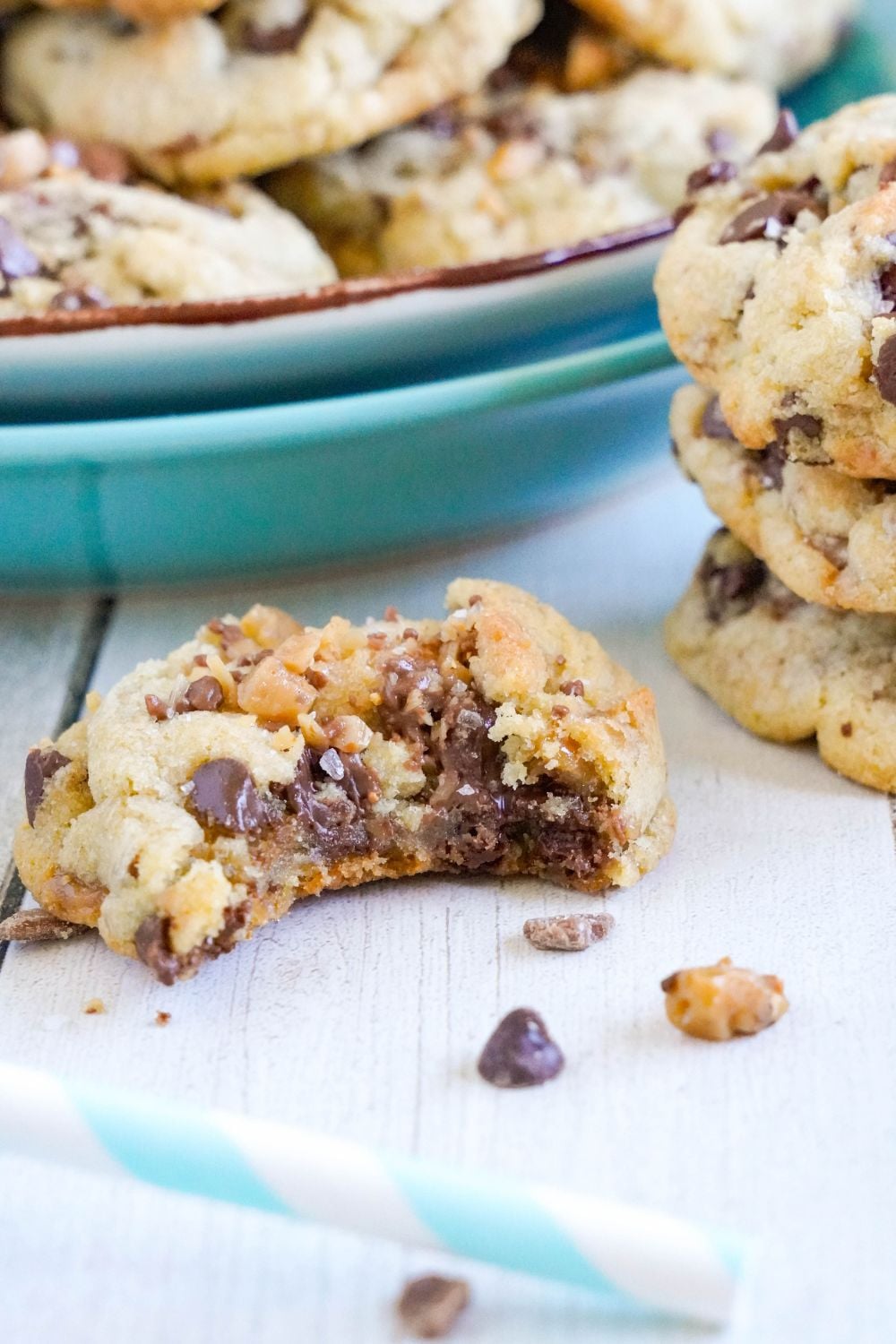 cookie with a bite taken out and a plate of Chocolate Chip Toffee Cookies around table