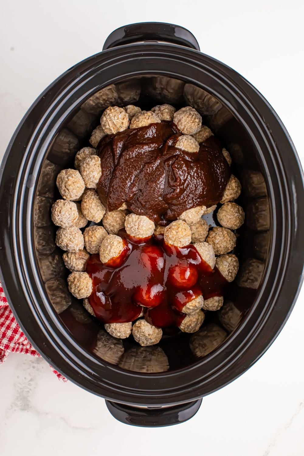 frozen meatballs with apple butter and bbq sauce poured over the top sitting in a slow cooker on table